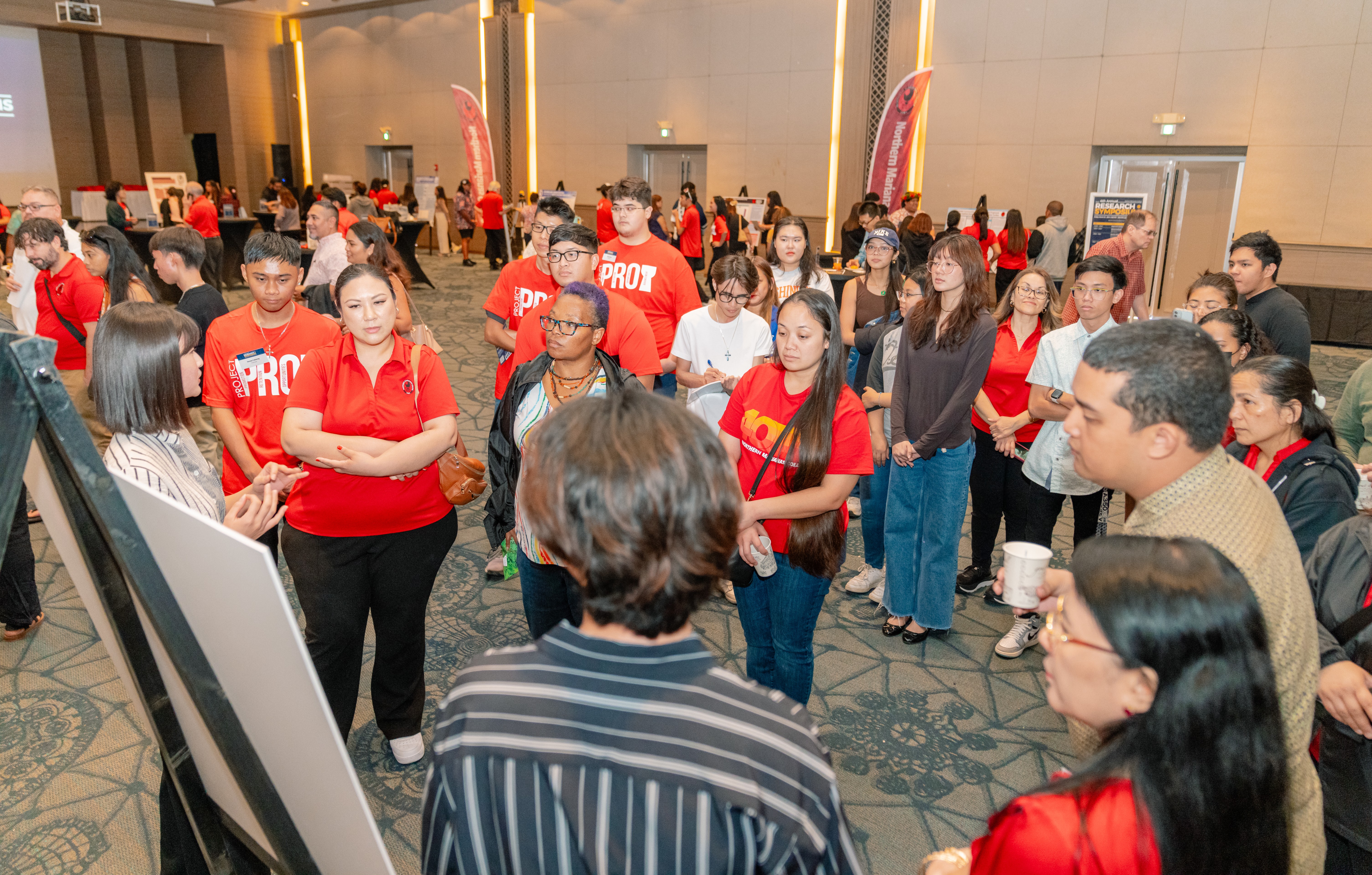 Attendees gather around NMC students Jun You and Cloie Seo, presenting their research.