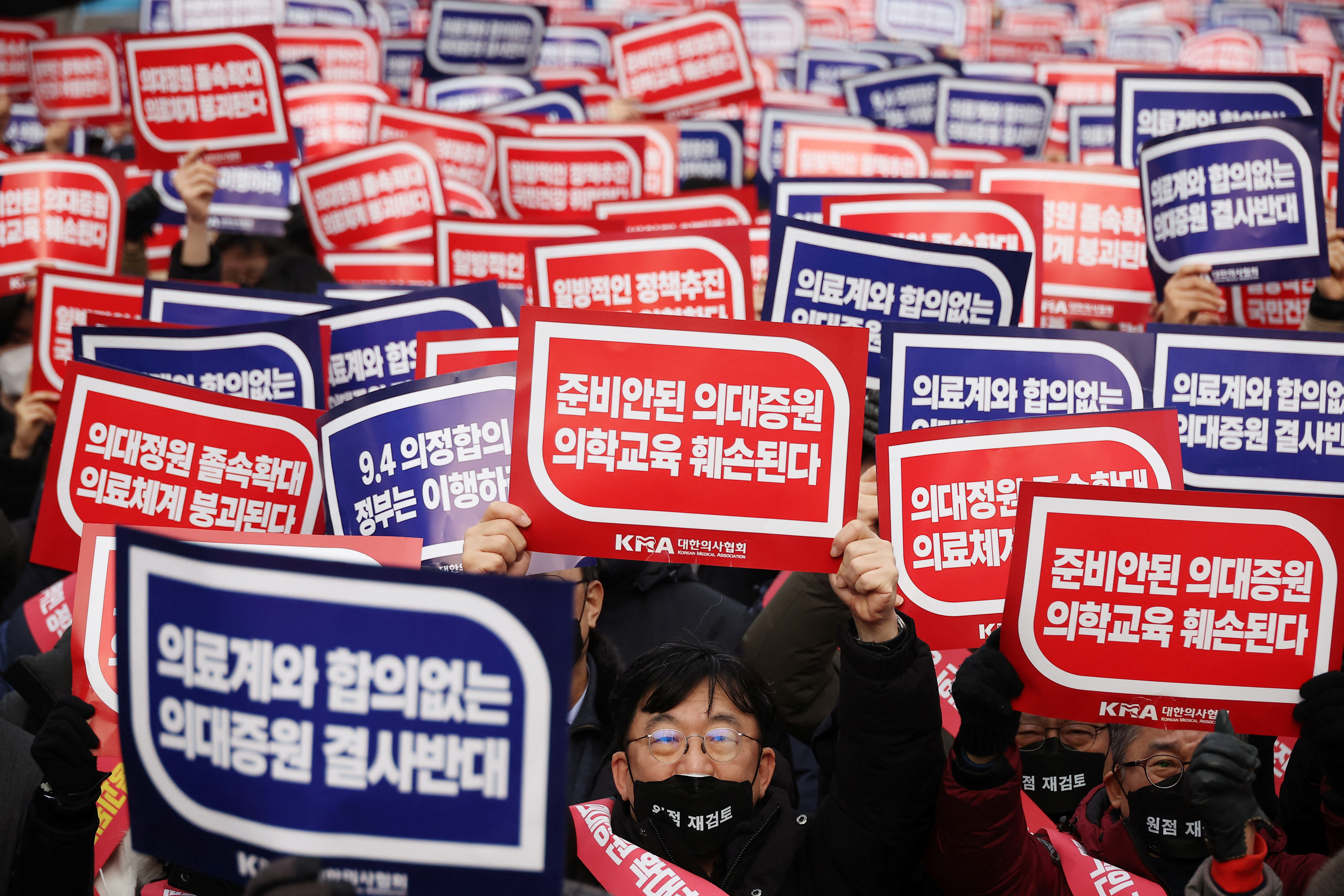 Doctors chant slogans during a rally to protest against government plans to increase medical school admissions in Seoul, South Korea, March 3, 2024. The banners read "Oppose increasing medical school admissions without talks with the medical community" (in blue) and "Medical education will be harmed in increasing medical school admissions" (in red). 