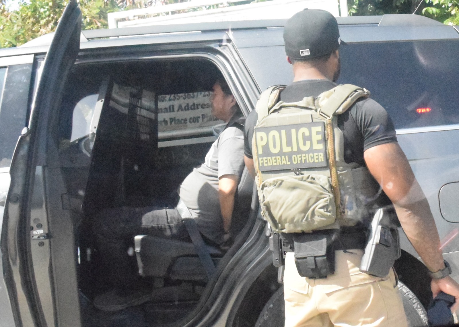 Fuquan Miao is seen in handcuffs inside an open vehicle, while a U.S. Marshals Service task force officer stands guard.