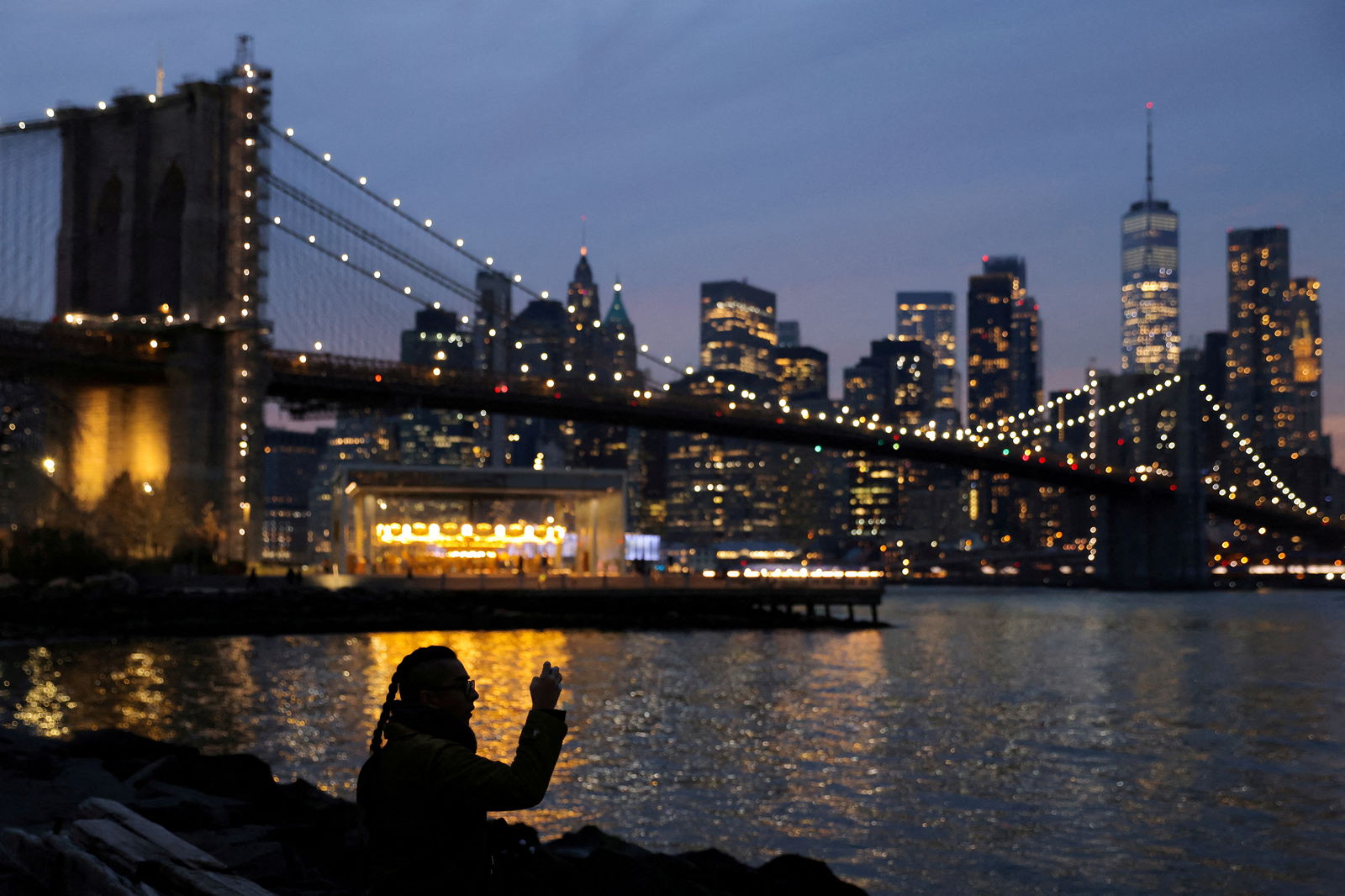 A person takes a photo while looking toward the Manhattan skyline on the Winter Solstice in Brooklyn, New York City, Dec. 21, 2021.