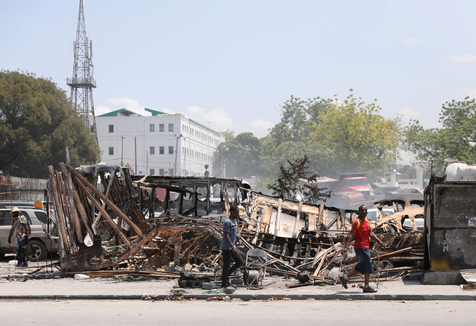 FILE PHOTO: People walk past remains of vehicles near the presidential palace, after they were set on fire by gangs, as violence spreads and armed gangs expand their control over the capital, in Port-au-Prince, Haiti March 25, 2024. 