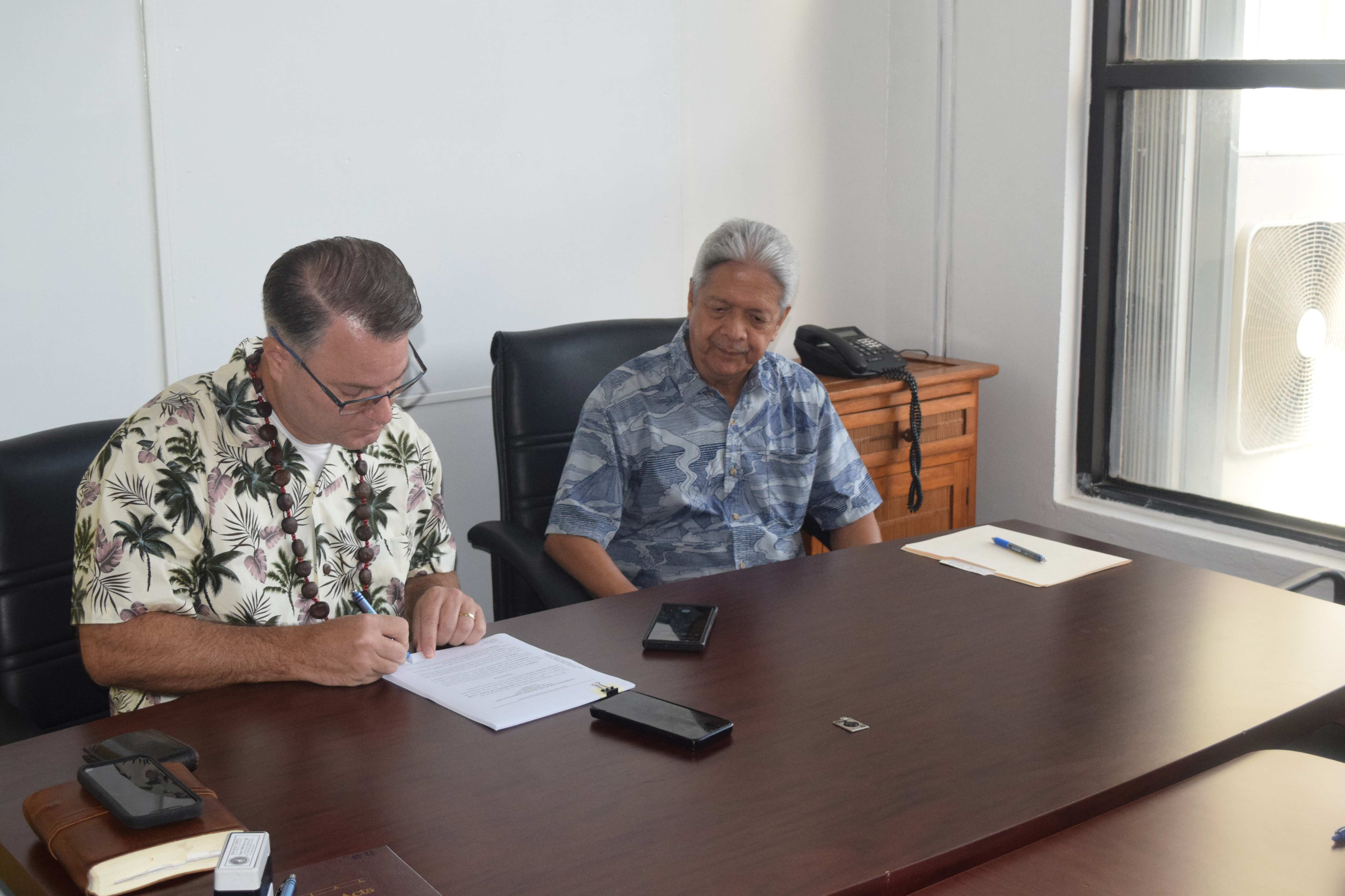 Grace Christian Academy Pastor Michael Rodgers signs a new land lease contract as Special Adviser for Department of Public Lands David Sablan looks on in the DPL conference room on Friday.