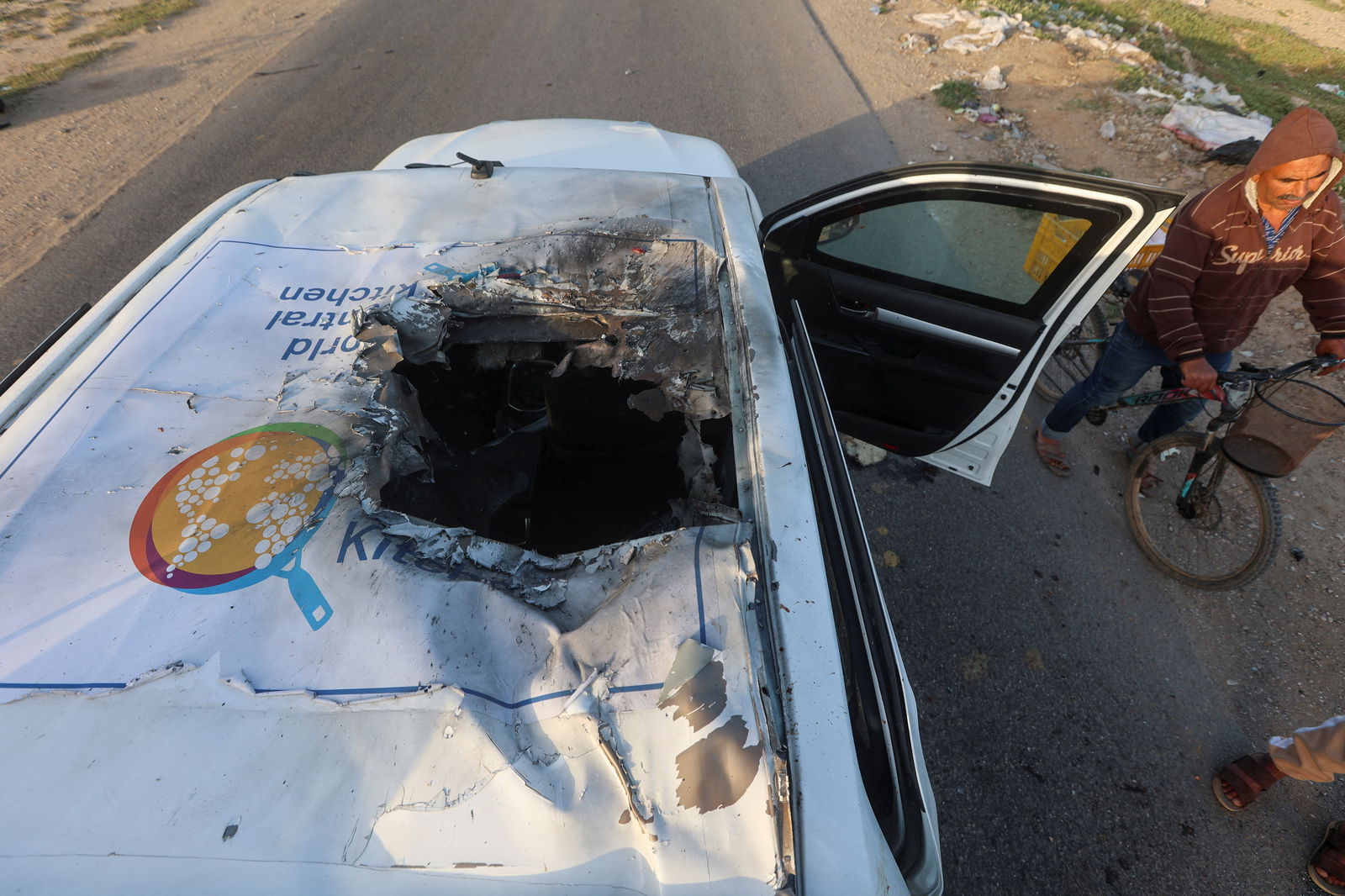 A Palestinian man rides a bicycle past a damaged vehicle where employees from the World Central Kitchen (WCK), including foreigners, were killed in an Israeli airstrike, according to the NGO as the Israeli military said it was conducting a thorough review at the highest levels to understand the circumstances of this "tragic" incident, amid the ongoing conflict between Israel and Hamas, in Deir Al-Balah, in the central Gaza, Strip April 2, 2024. 