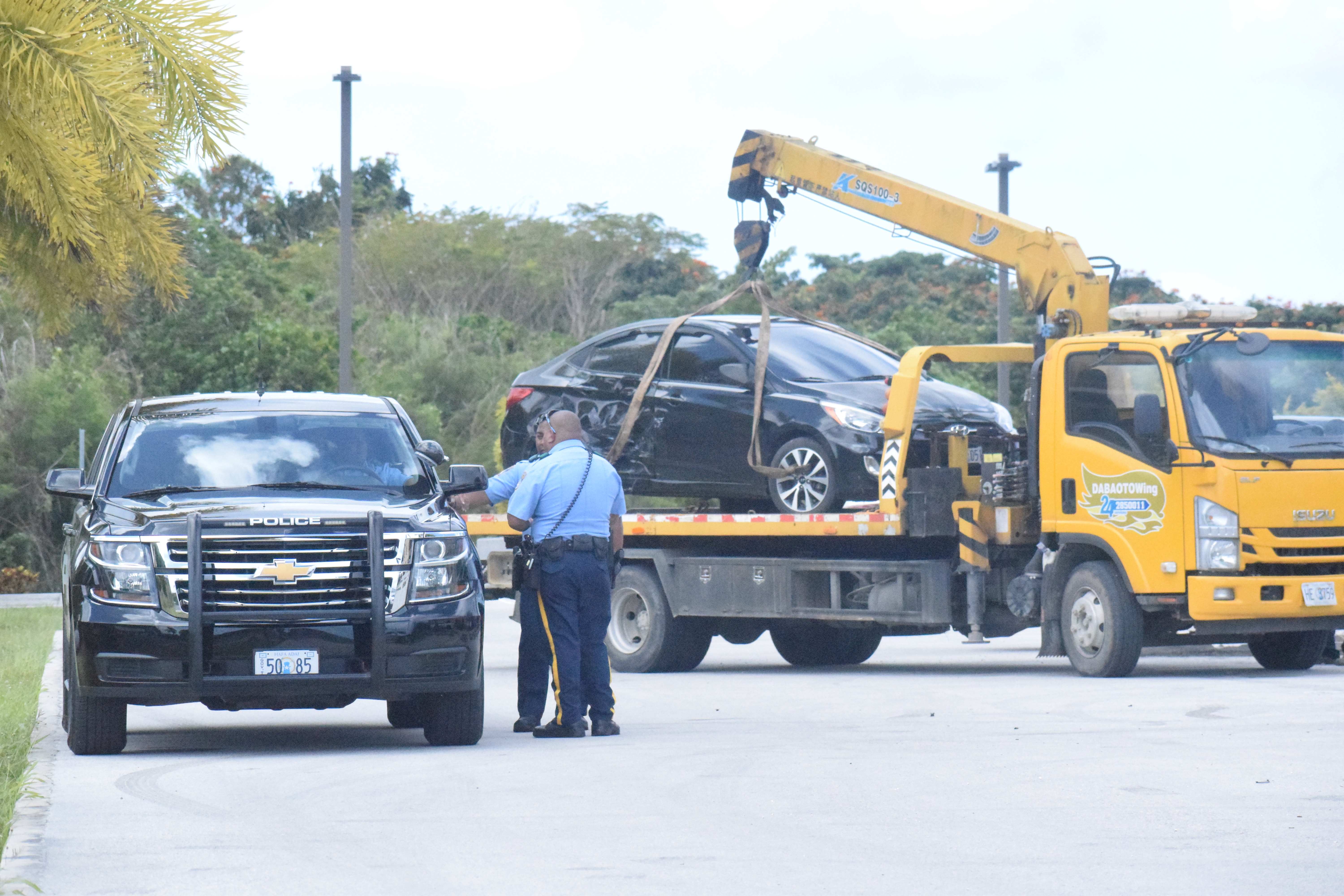 Responding police officers confer as one of the cars damaged by a motorist is towed from the parking lot of the United States Courthouse in Gualo Rai on Thursday.