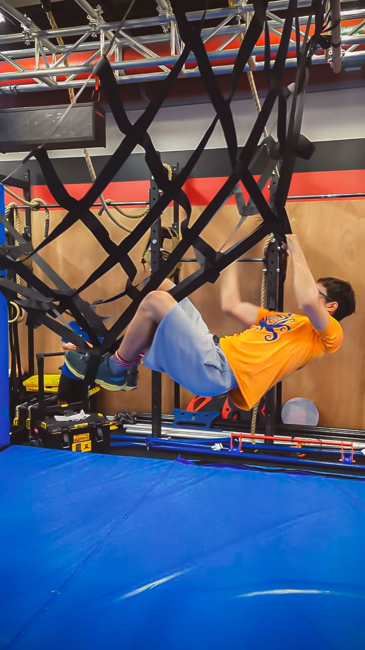 An athlete uses hands and feet to grab on to cargo net in a Sindalu Ninja Games demonstration.