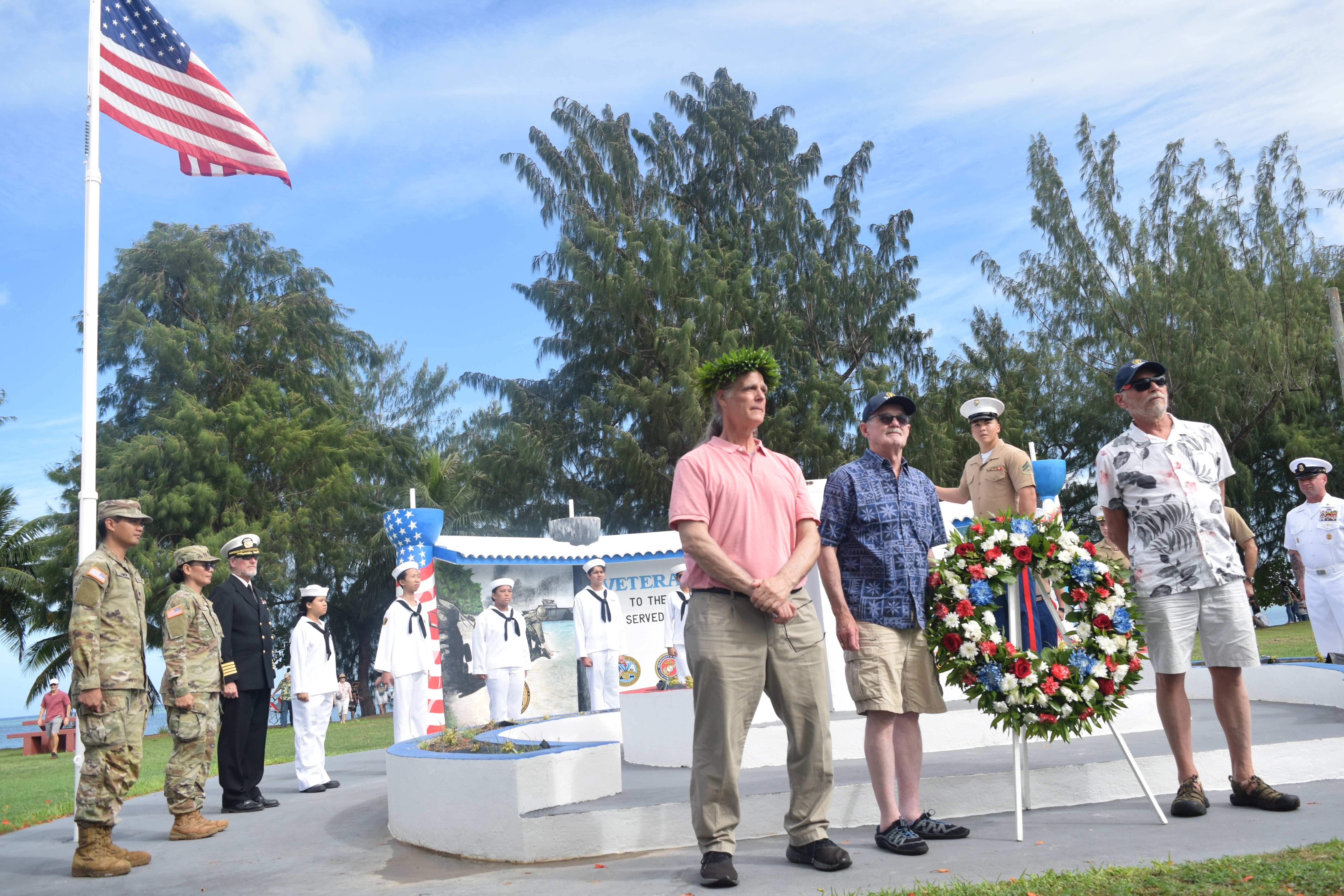 William Michels Jr., Jack Padley and Dave Knisley pose next to a wreath at a memorial at Invasion Beach in Susupe. Also in photo are the Marines and the Western Pacific Maritime Academy cadets led by Executive Director Capt. Michael W. Bacher.
