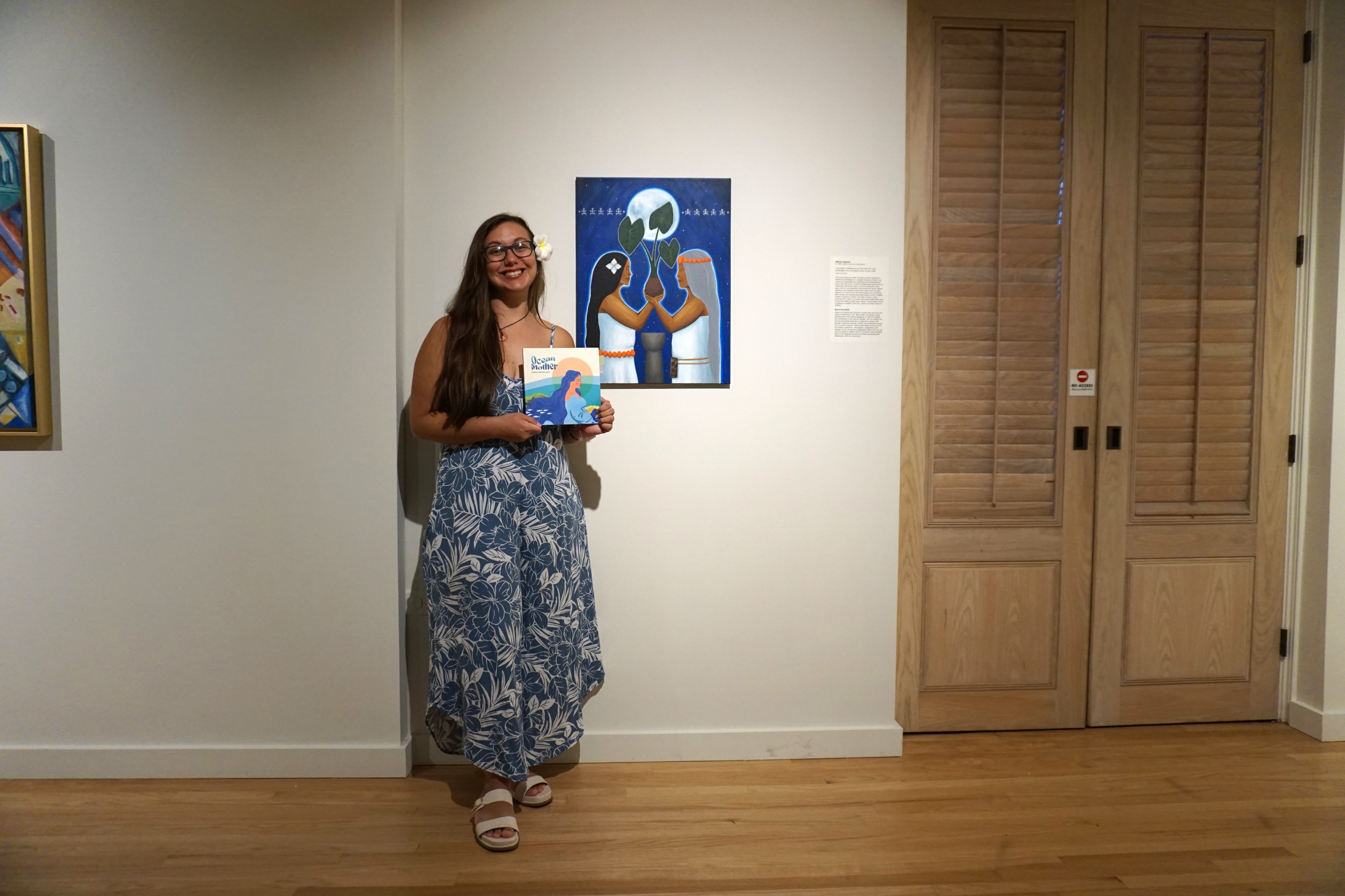 Arielle Taitano Lowe holds a copy of her debut book of poetry as she poses for a photo near Gillian Duenas' artwork, “I menhalom manaina-ta na man la'la' hit” at Capitol Modern in Honolulu, Hawaii on June 14.