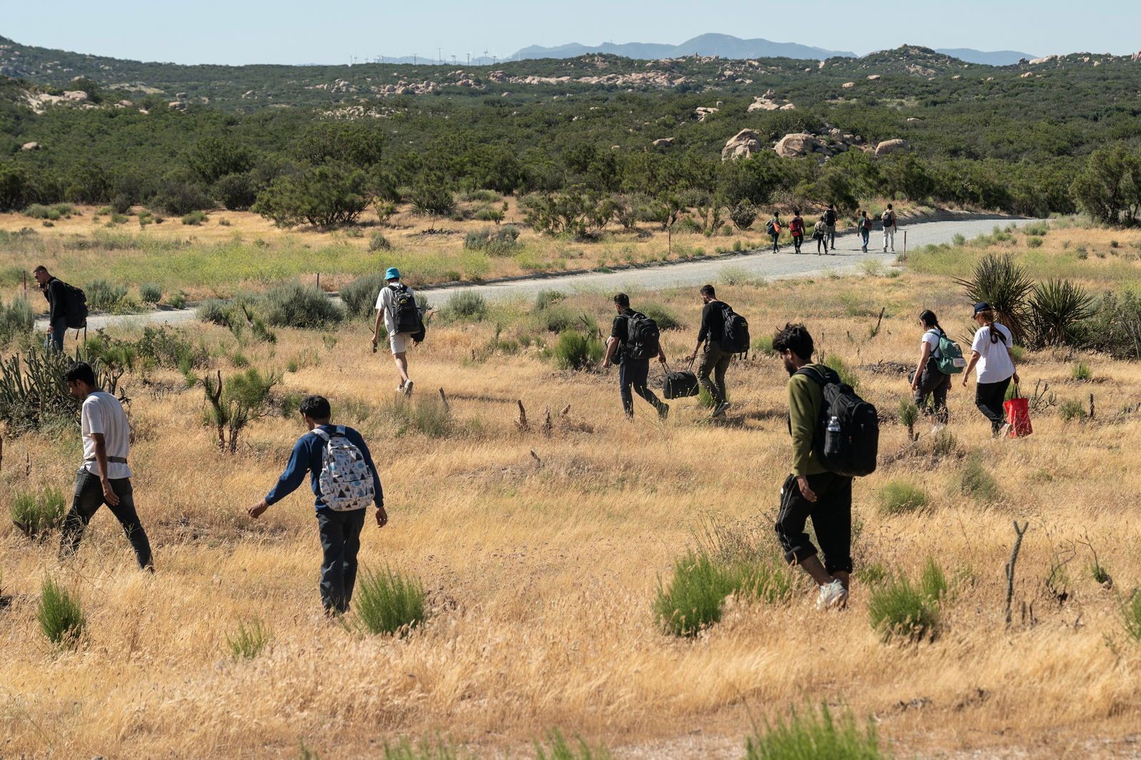 Asylum-seeking migrants walk near the border to leave a temporary staging area to be transported, after President Joe Biden announced a sweeping border security enforcement effort, in Jacumba Hot Springs, California, June 4, 2024.