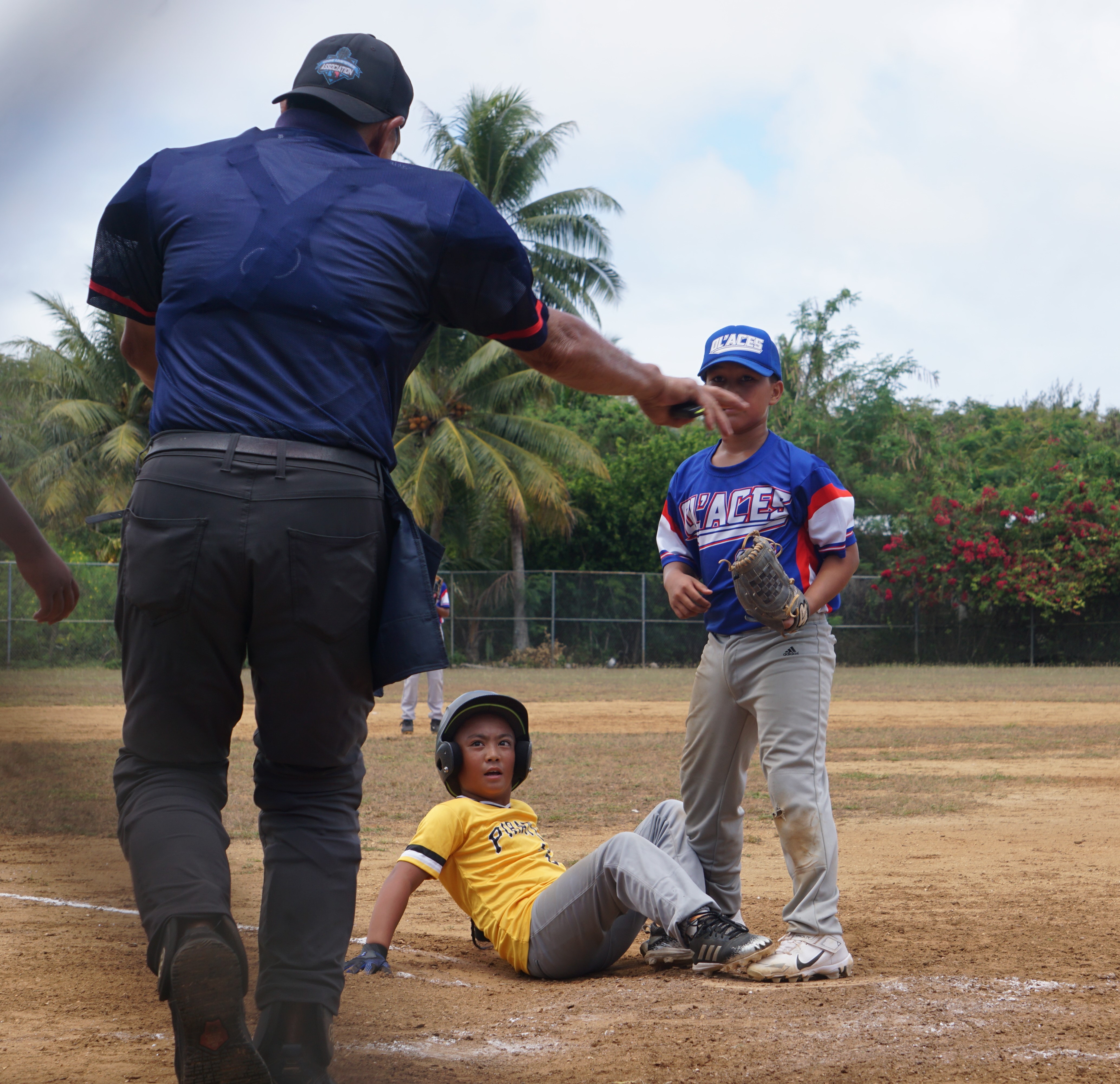 The umpire calls safe as a Pirate slides home to beat the tag during a game against the Ol'Aces in the majors division of the 2024 NSA Youth Baseball League at the Miguel "Tan Ge" Pangelinan Baseball Field.