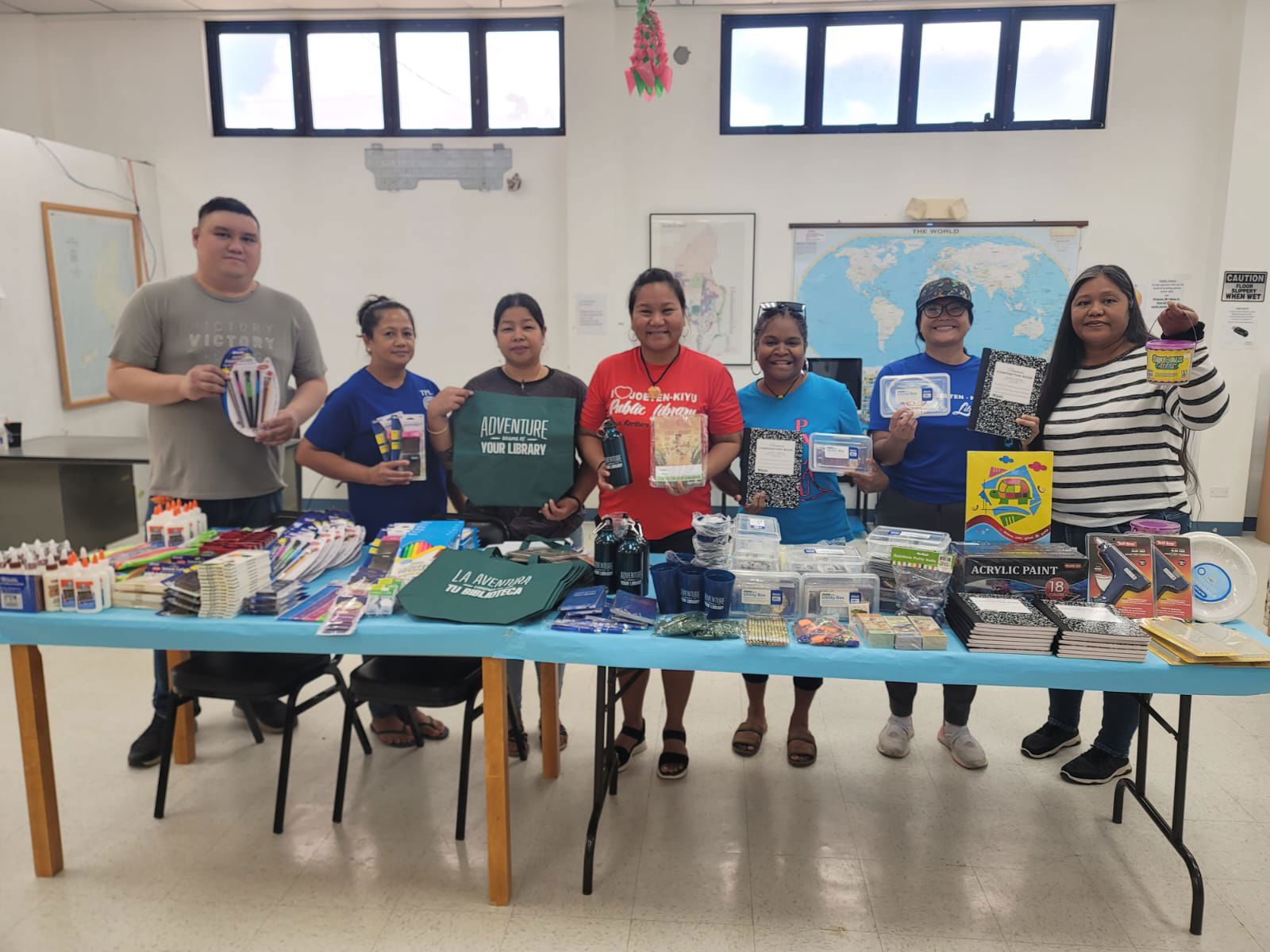 Team JKPL with Tinian Public Library staff displaying summer reading program supplies.