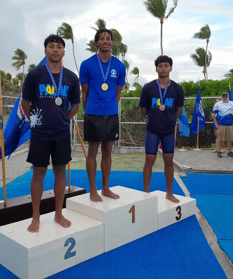 The NMI’s Isaiah Aleksenko, center, leads the podium finishers in the 50yd butterfly race.