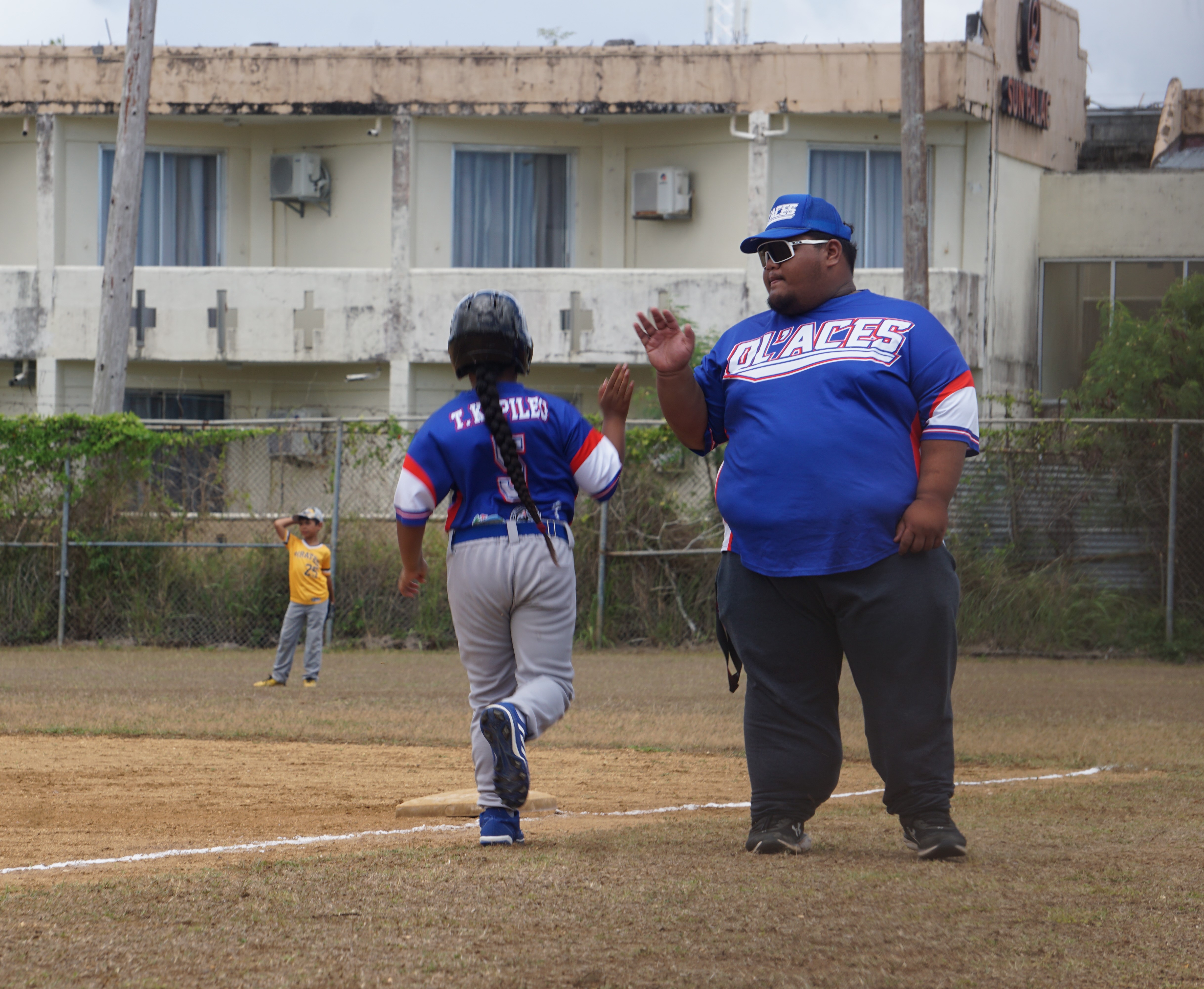 Ol'Aces' Tioni Kapileo high-fives his coach as he makes his way to first base safely during a majors division game of the 2024 NSA Youth Baseball League at the Miguel "Tan Ge" Pangelinan Baseball Field.