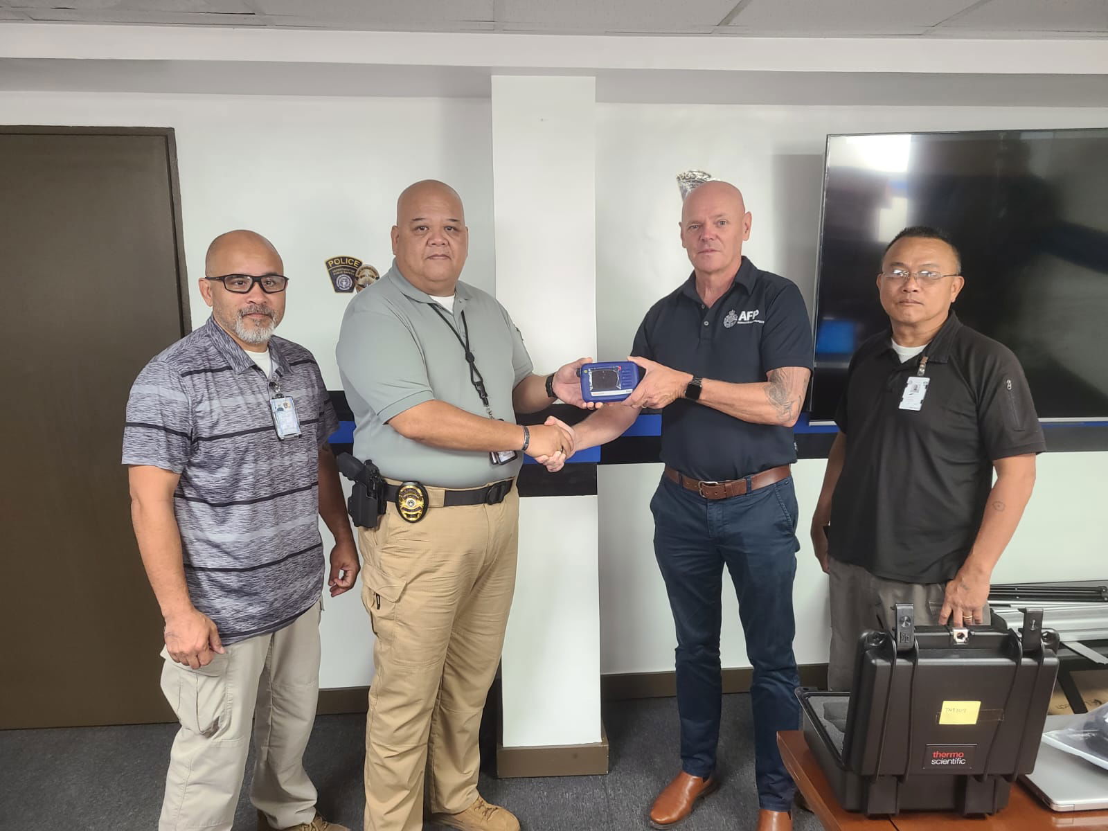 Detective Sergeant Jason Ford from the Australian Federal Police, 2nd right, hands a TruNarc Handheld Narcotics Analyzer to Department of Public Safety Commissioner Anthony I. Macaranas.