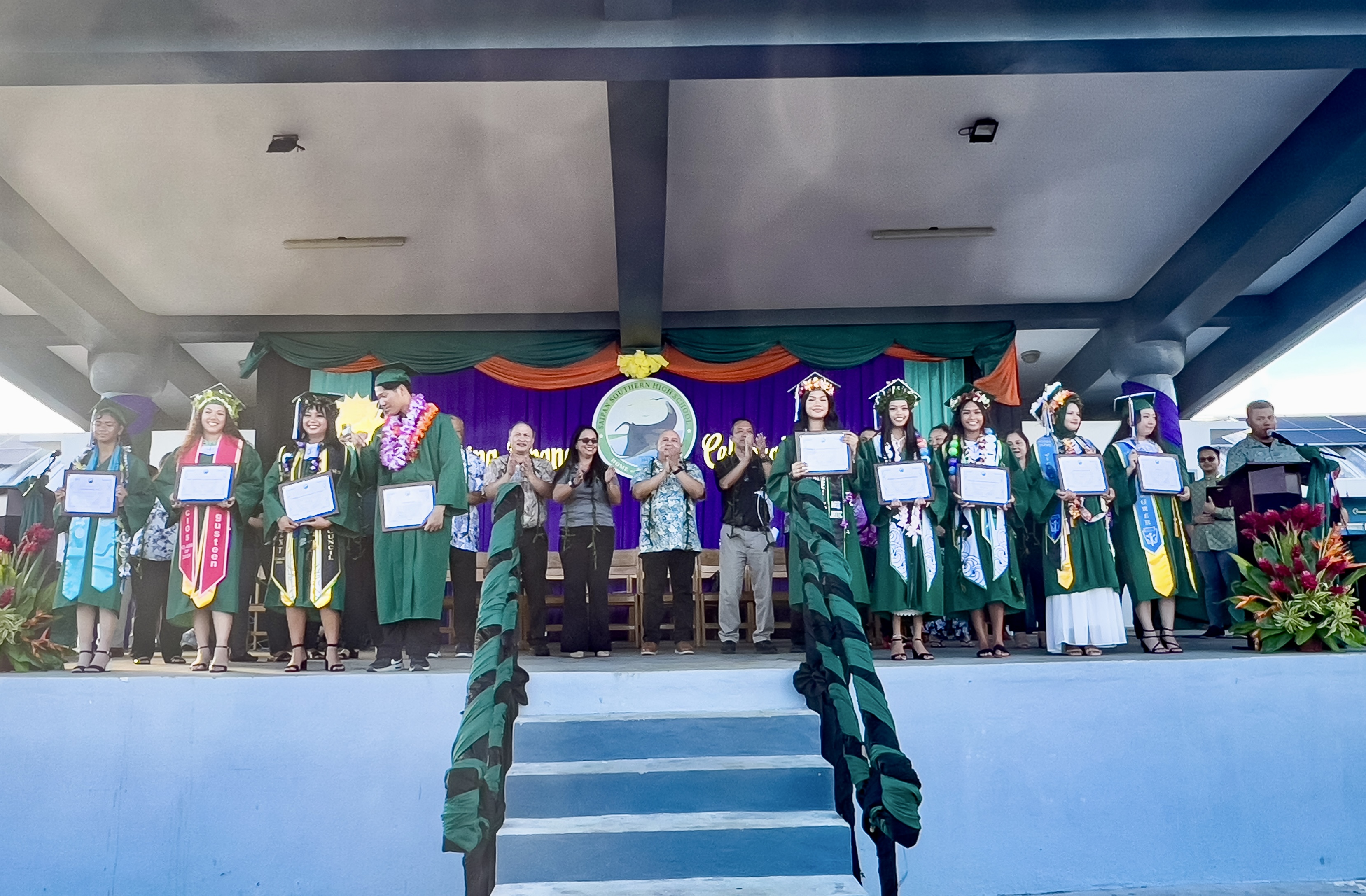 Saipan Southern High School’s Class of 2024 top 10 graduates: (1) valedictorian Ye Zhi Sablan (not in photo), (2) salutatorian Jing Lin, (3) Shamira Sulyman, (4) Gracie Reign Ordonez Mendiola, (5) Jobelle Ann Gutirre Sapo, (6)Jasmine Kyle Materum Saluta, (7) Uirom Park, (8) Aleeza Jolia Taitingfong Castro, (9) Sky Gusteen Lizama Palacios, and (10) Fatima Rose Ito. They are joined on stage by education officials led by Acting Board of Education Chair Maisie B. Tenorio, BOE member Andrew L. Orsini and Commissioner of Education Dr. Lawrence F. Camacho.