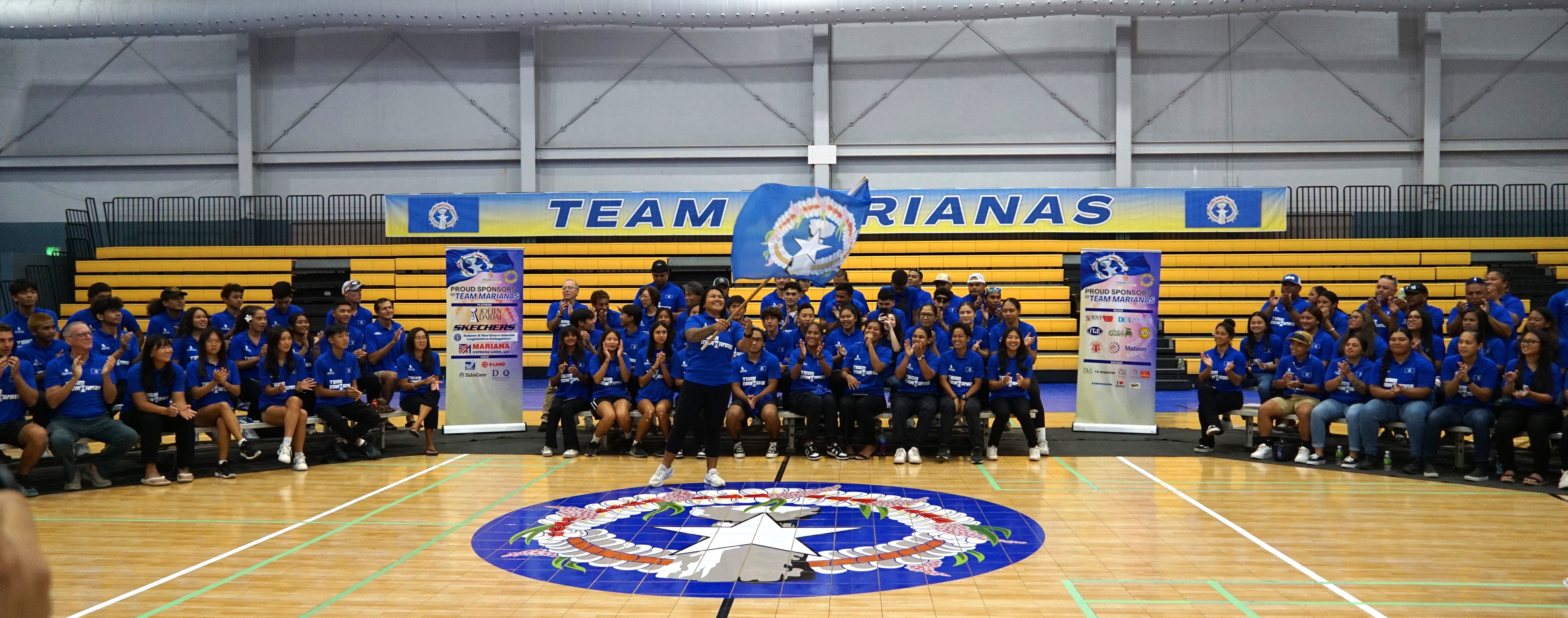Antonette Labausa, center standing, waves the CNMI flag at the send-off ceremony at the Ada gym on Monday after being selected as Team Marianas’ flagbearer for the 2024 Micronesia Games
