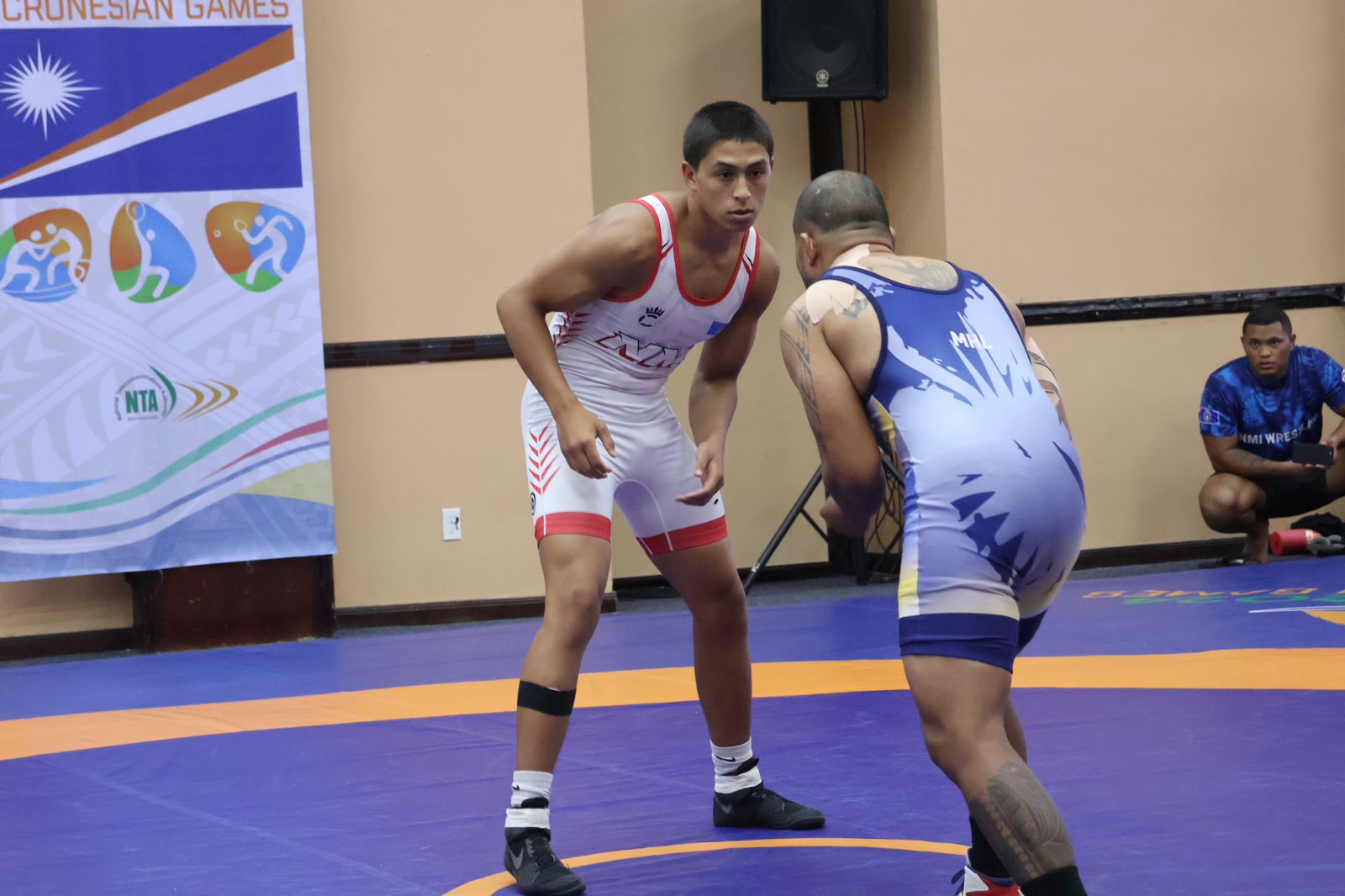 The NMI’s James Attao-Greene Jr., left, seizes up his opponent from the Marshall Islands, while fellow NMI wrestler Ryan Babauta looks on.