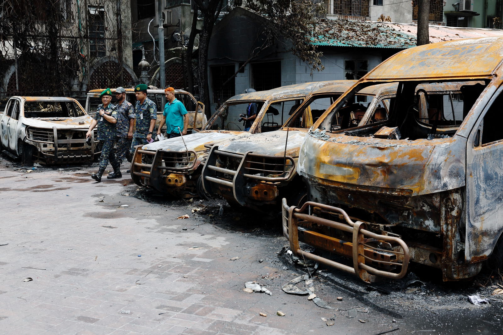 Security personnel walk past damaged vehicles of a government owned organization that were set afire by a mob during clashes after violence erupted following protests by students against government job quotas, in Dhaka, Bangladesh, July 22, 2024.