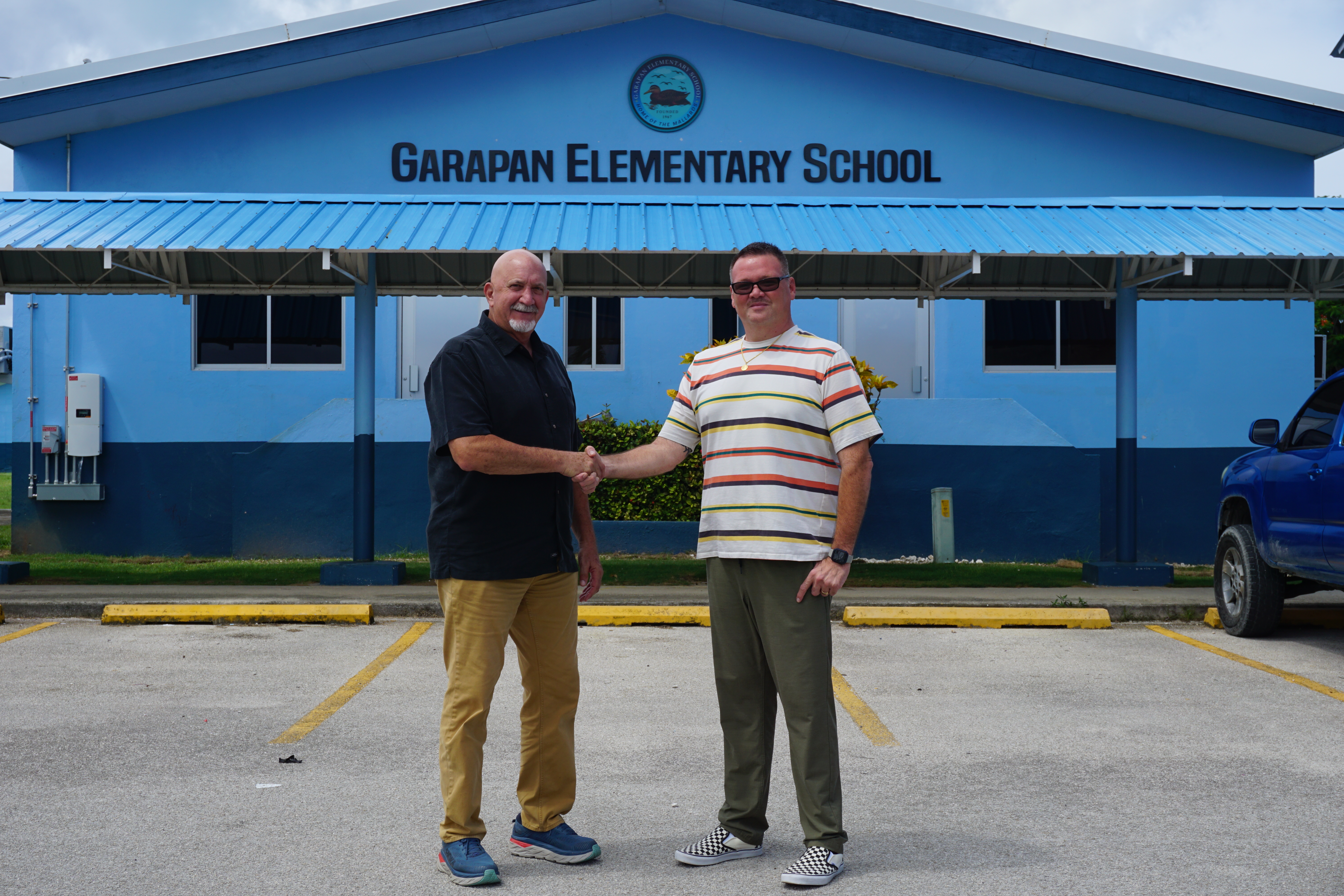 Bridge Capital LLC Vice President Bart Jackson left, and Garapan Elementary School Principal Derwin Johnson shake hands in front of the new signage donated by Bridge Capital LLC.