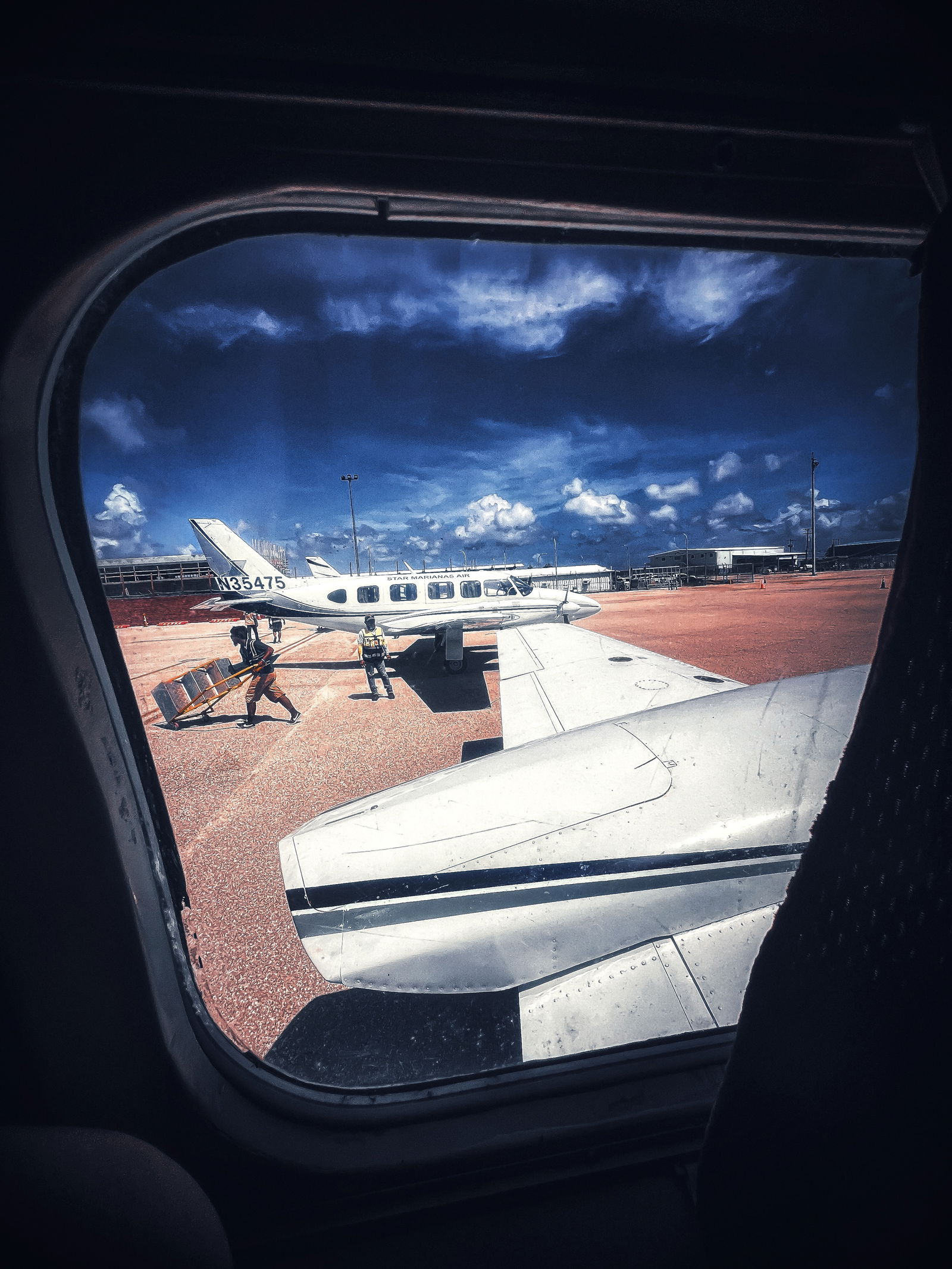 A photo taken through a window of a Piper PA-31-350 Navajo Chieftain shows ground crew members of Star Marianas Air at work at the Francisco C. Ada/Saipan International Airport.