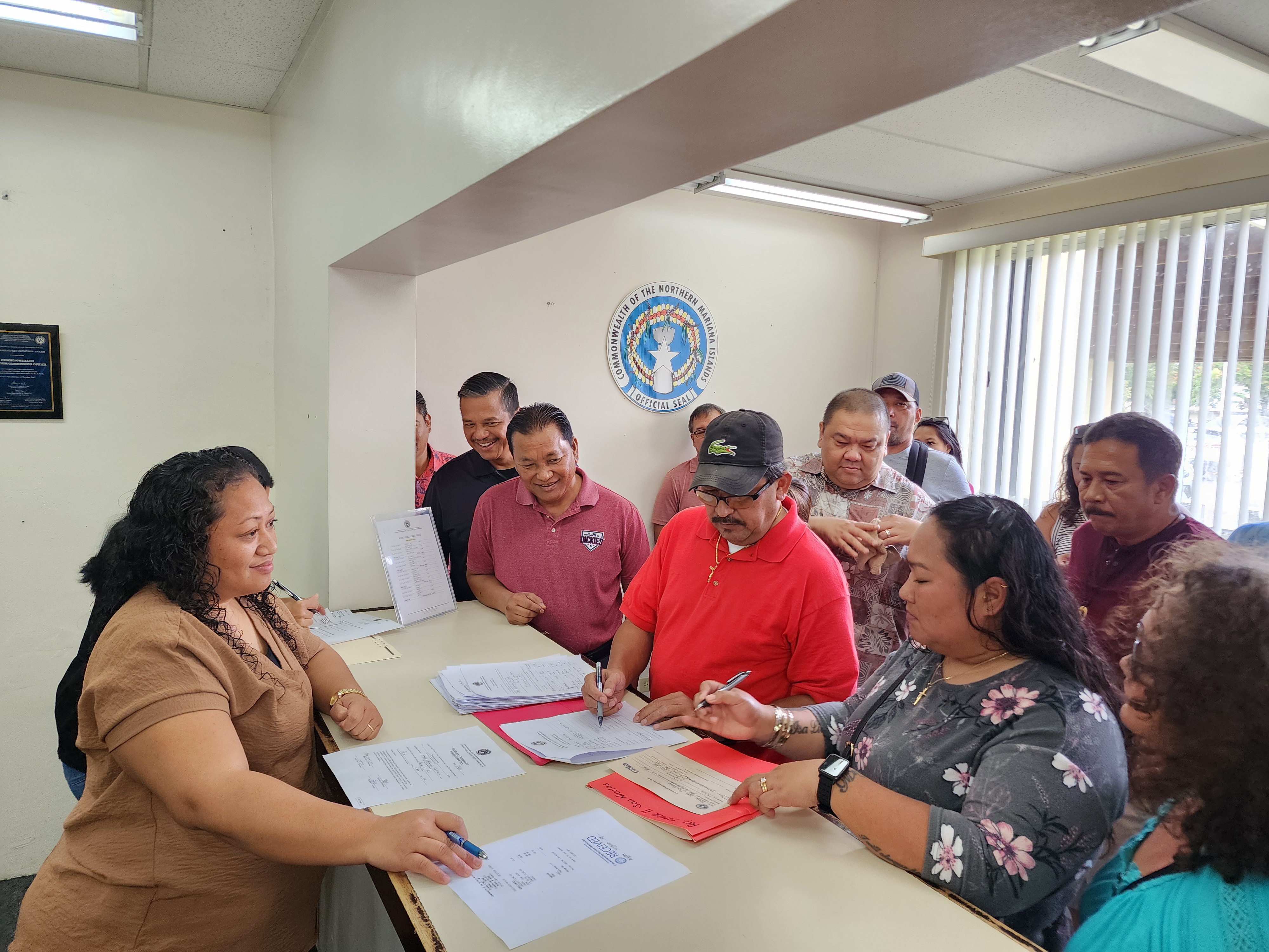 Commonwealth Election Commission Executive Director Kayla Igitol, left, receives official documents from Tinian Rep. Patrick San Nicolas, who was with his family members and other supporters as he filed his candidacy Friday morning.