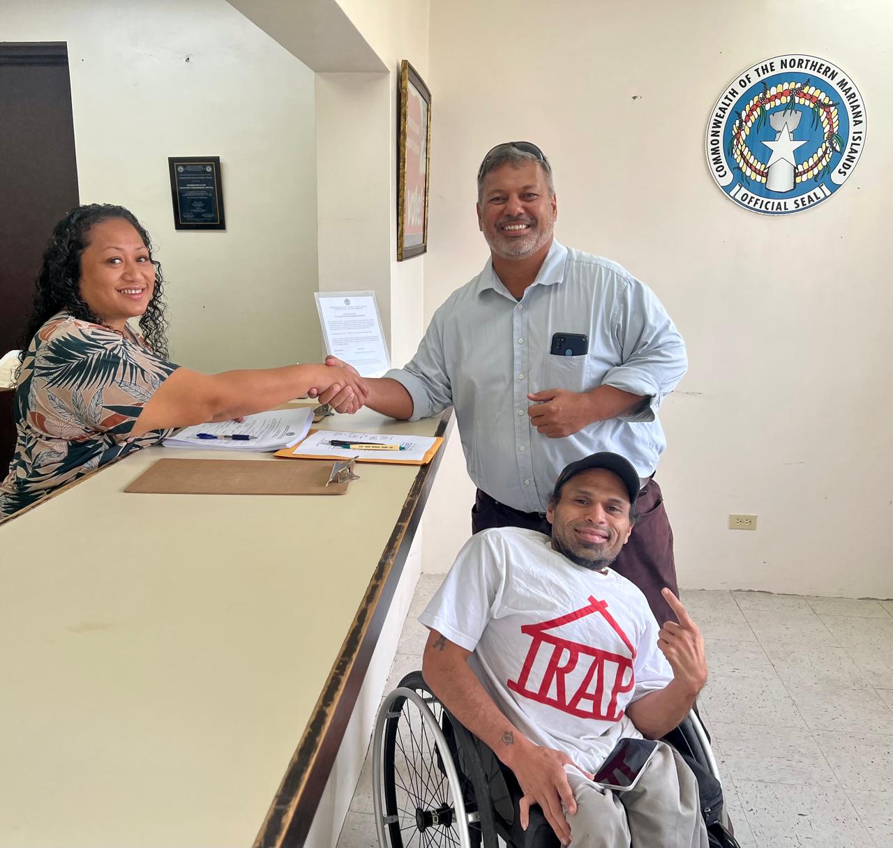 U.S. congressional candidate James M. Rayphand, right standing, shakes hands with Commonwealth Election Commission Executive Director Kayla Igitol. Also in photo is his treasurer, John Cabrera. Not in photo: Monissalyn I. Blas, the campaign chair.