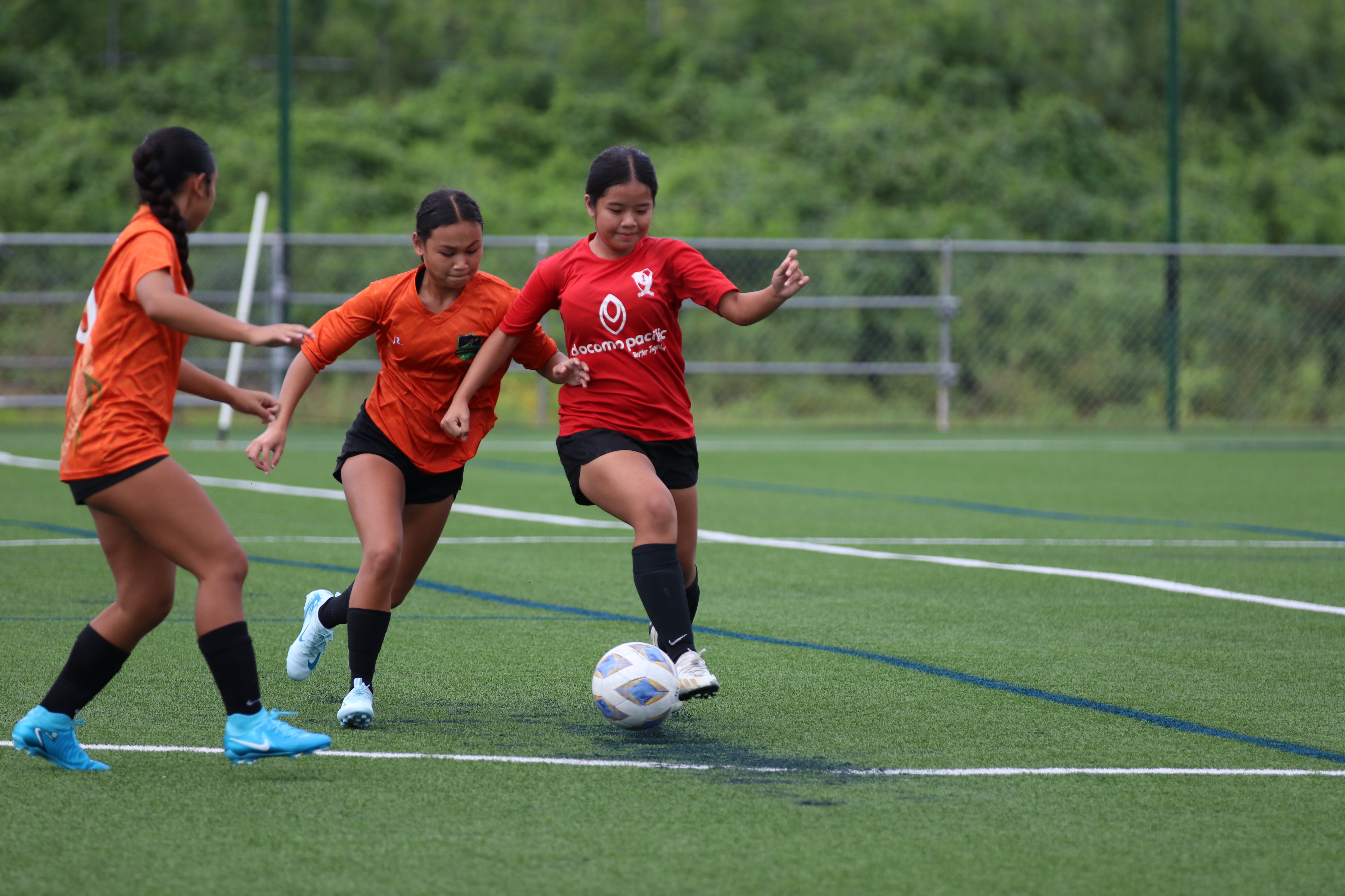 A Paire FC player runs past Kanoa FC defenders during a U14 Girls Division game.