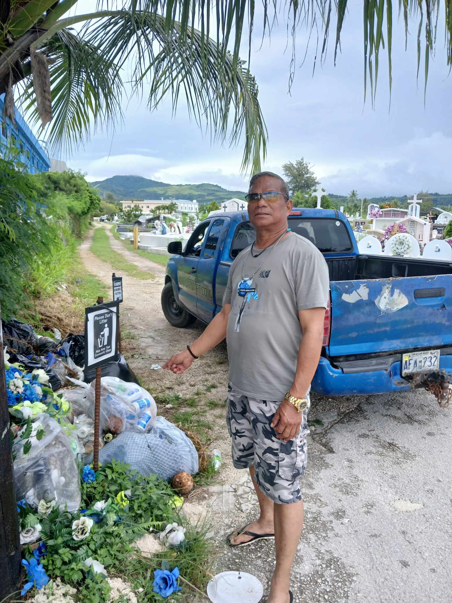 Max Aguon points to illegally dumped household trash at the Chalan Kanoa cemetery.