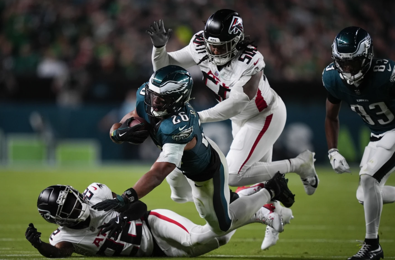Philadelphia Eagles running back Saquon Barkley (26) falls with the ball near Atlanta Falcons cornerback Clark Phillips III, bottom, and defensive end James Smith-Williams during the second half of an NFL game Monday, Sept. 16, 2024 in Philadelphia.