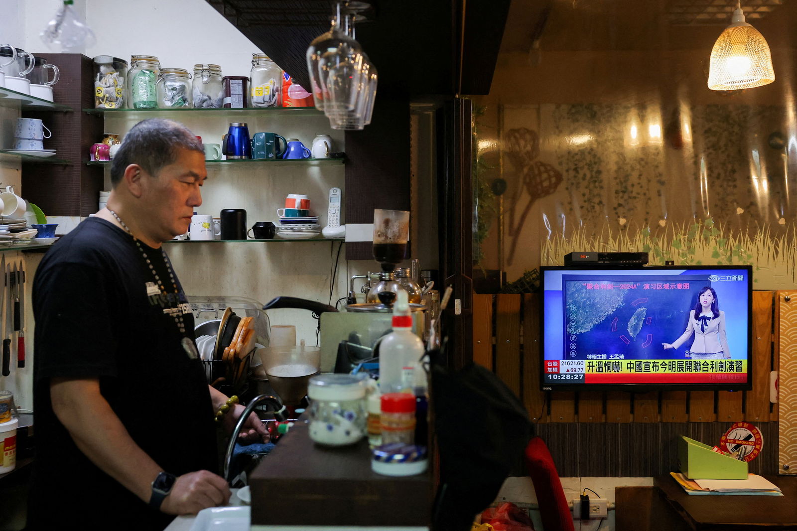 A man stands in a café as a news broadcast shows China announcing new military drills around Taiwan, in Keelung, Taiwan, May 23, 2024.