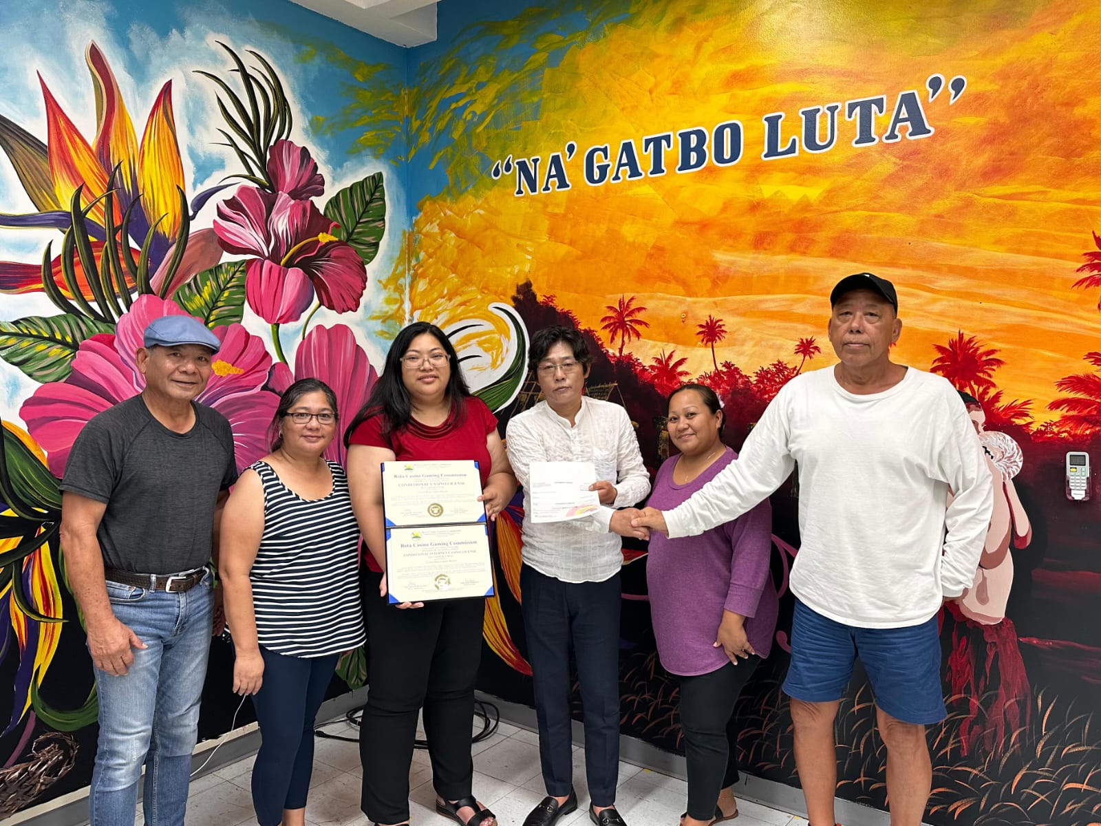 Rota Mayor Aubry Hocog, third left, and IH Group Chairman Kyunam Kim, third right, holds a copy of a Rota casino license as they pose for a photo with Rota Gaming Commission Chair Mateo Santos, right, and other gaming commissioners.