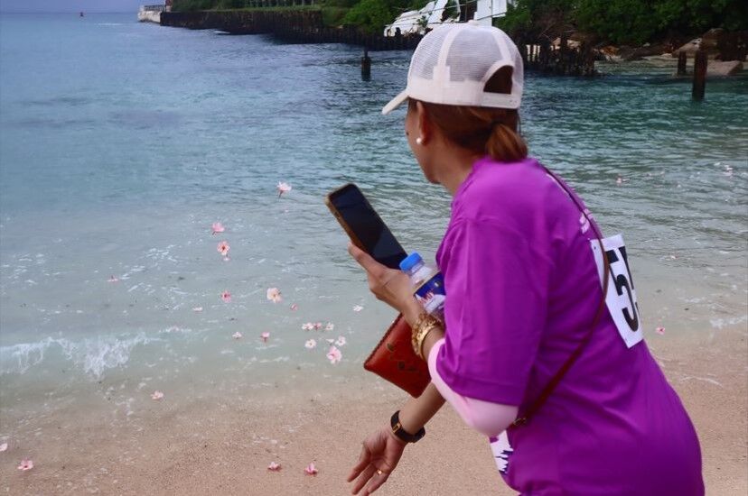 A community member throws plumerias into the ocean to honor those who struggled with domestic & sexual violence and breast cancer.