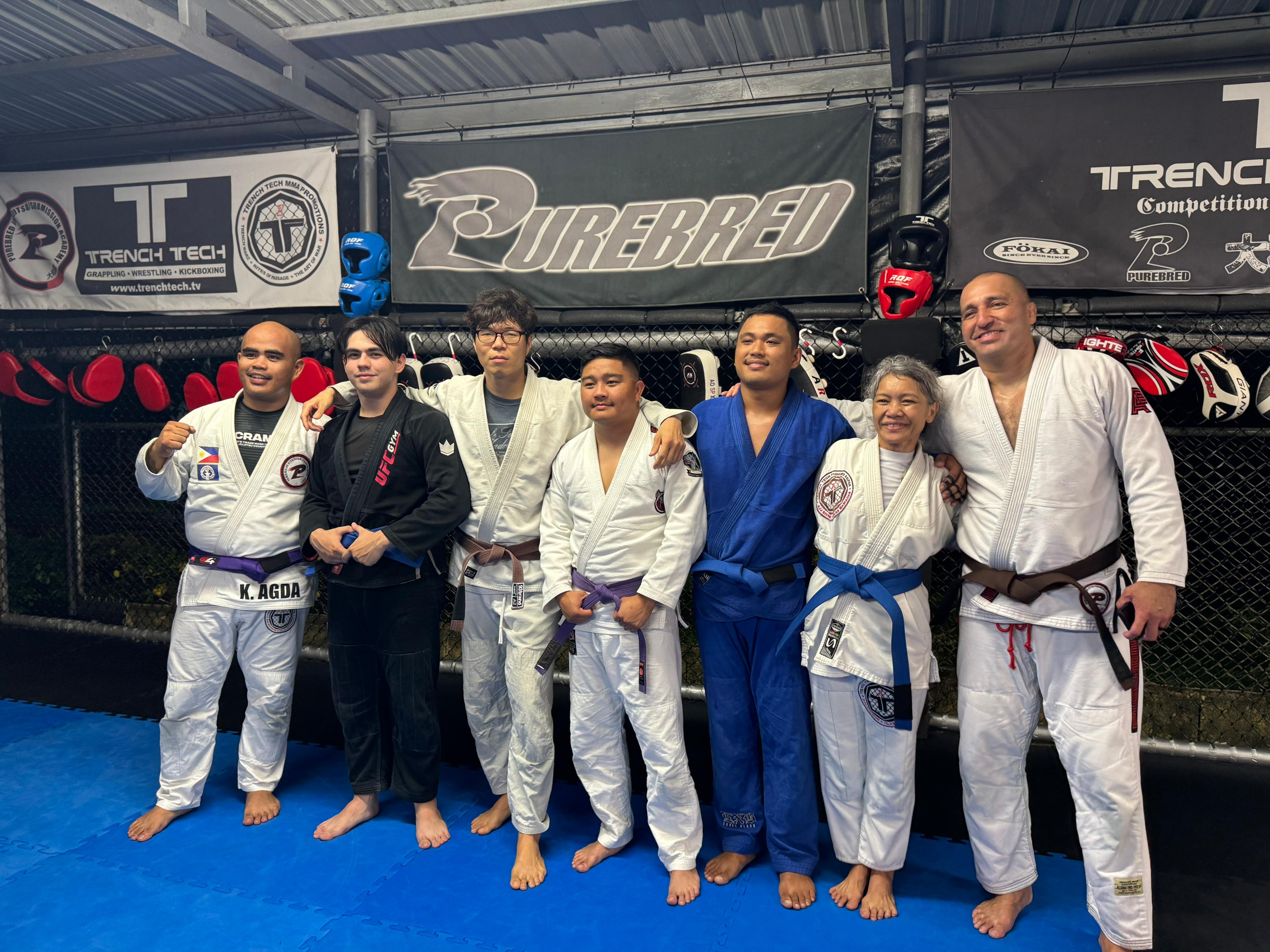 The belt promotees — Kier Agda (Purple), Isaiah Sablan (Blue), Giovanni Taitinfong (Purple), Jason Artero (Blue), Mariana Alvarez (Blue), and Mike Atoigue (Brown) — pose for a photo with Coach Rey Kim during a BJJ class at the Trench Tech gym on Thursday.