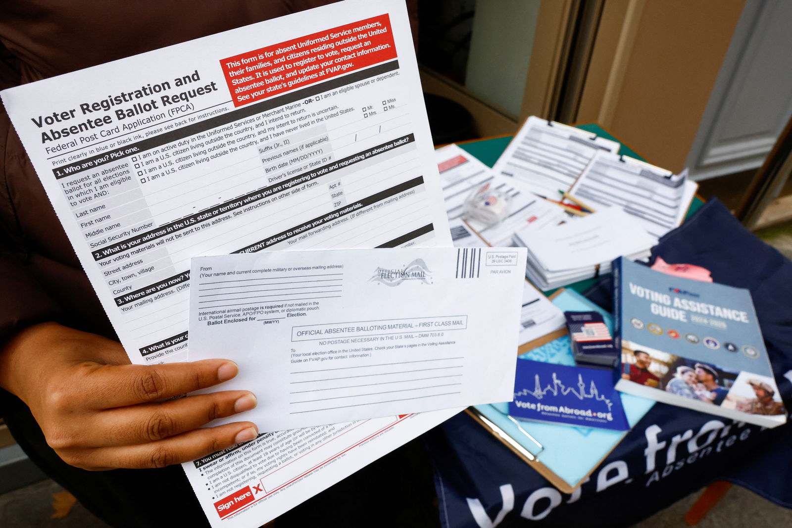 In this photo taken in Paris, France on Oct. 21, 2024, a U.S. citizen abroad  holds a voter registration and absentee ballot request form and an envelope, which will contain an official absentee balloting material, at a stand set up outside a café by Democrats Abroad volunteers to help Americans living in Paris to navigate the bureaucracies of state and local election laws.