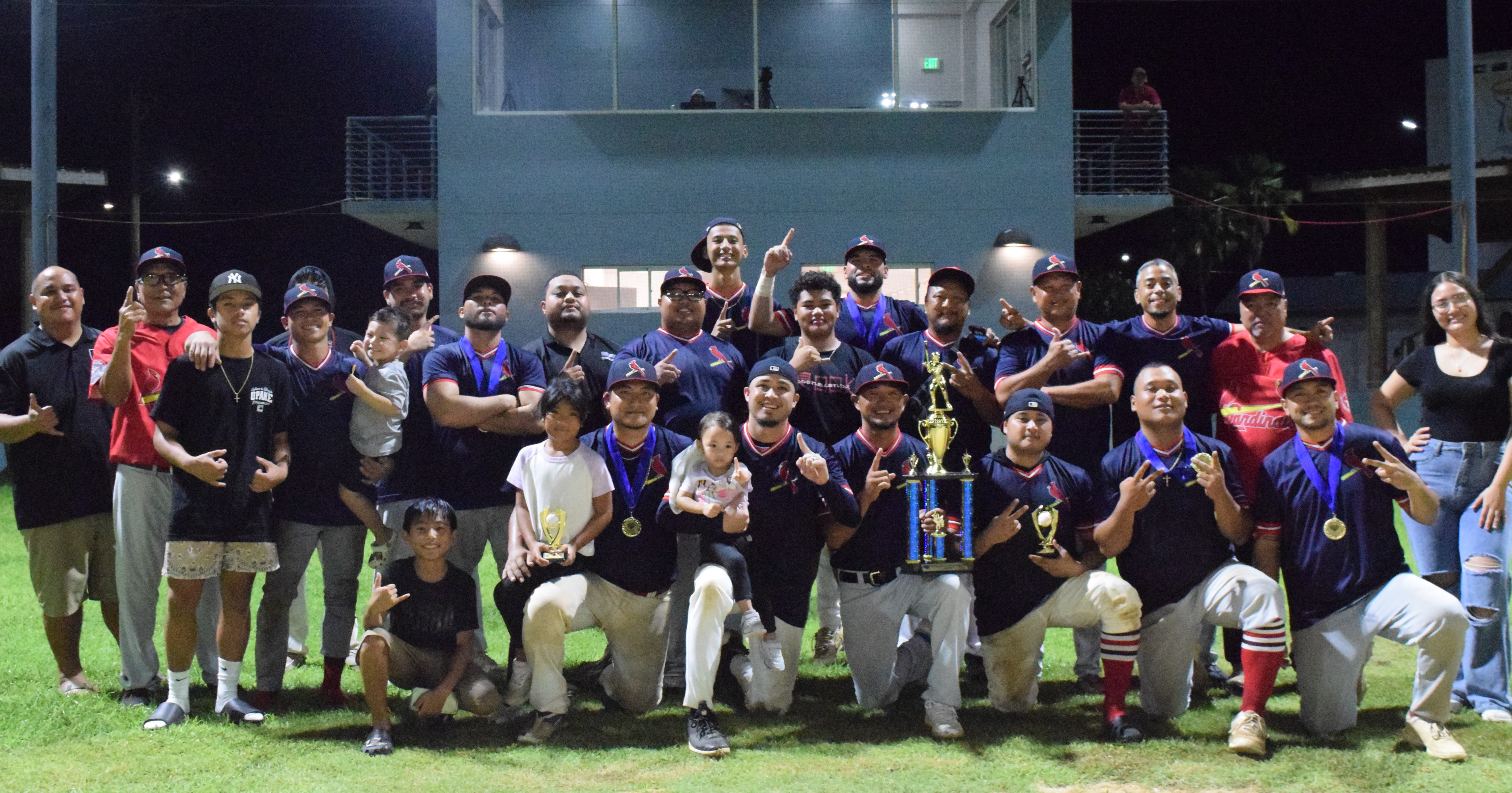 The 2024 Tan Holdings Saipan Baseball League champions, the Cardinals, and their family members pose for photo after the final game at the Francisco “Tan Ko” Palacios Baseball Field Monday night. Joining them is SBL board member Shine Tenorio, left.