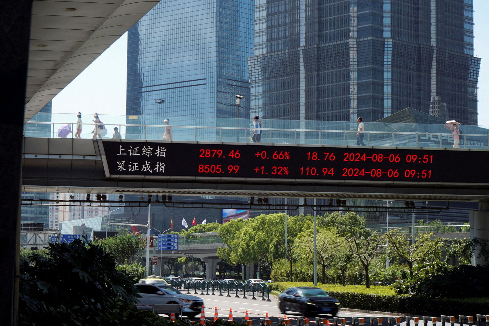 People walk on an overpass with a display of stock information in front of buildings in the Lujiazui financial district in Shanghai, China, Aug. 6, 2024.