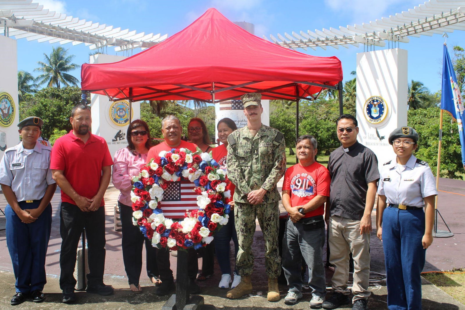 Tinian Mayor Edwin P. Aldan holds up Field of Heroes Memorial wreath alongside Ensign Jack Biersmith, Tinian 19th Municipal Council Secretary Estevan Cabrera, Tinian San Jose Church’s Rev. Father Brigido Bagunas, C/PFC Israt Syed, Mayor Aldan’s wife, Rosita King-Aldan, Tinian 19th Municipal Council Chair Joseph Santos, Joseph, C/PV2 Ken Litulumar, and representatives of the Tinian Mayor’s office.