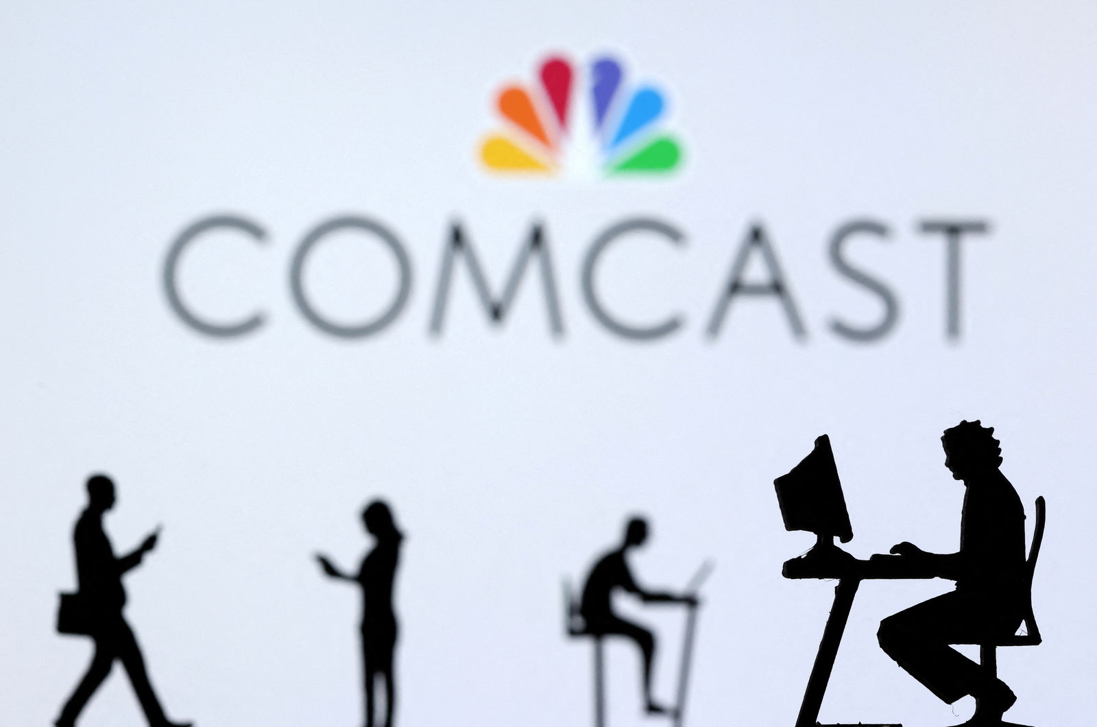 Small toy figures with laptops and smartphones are seen in front of displayed Comcast logo, in this illustration taken on Dec. 5, 2021.