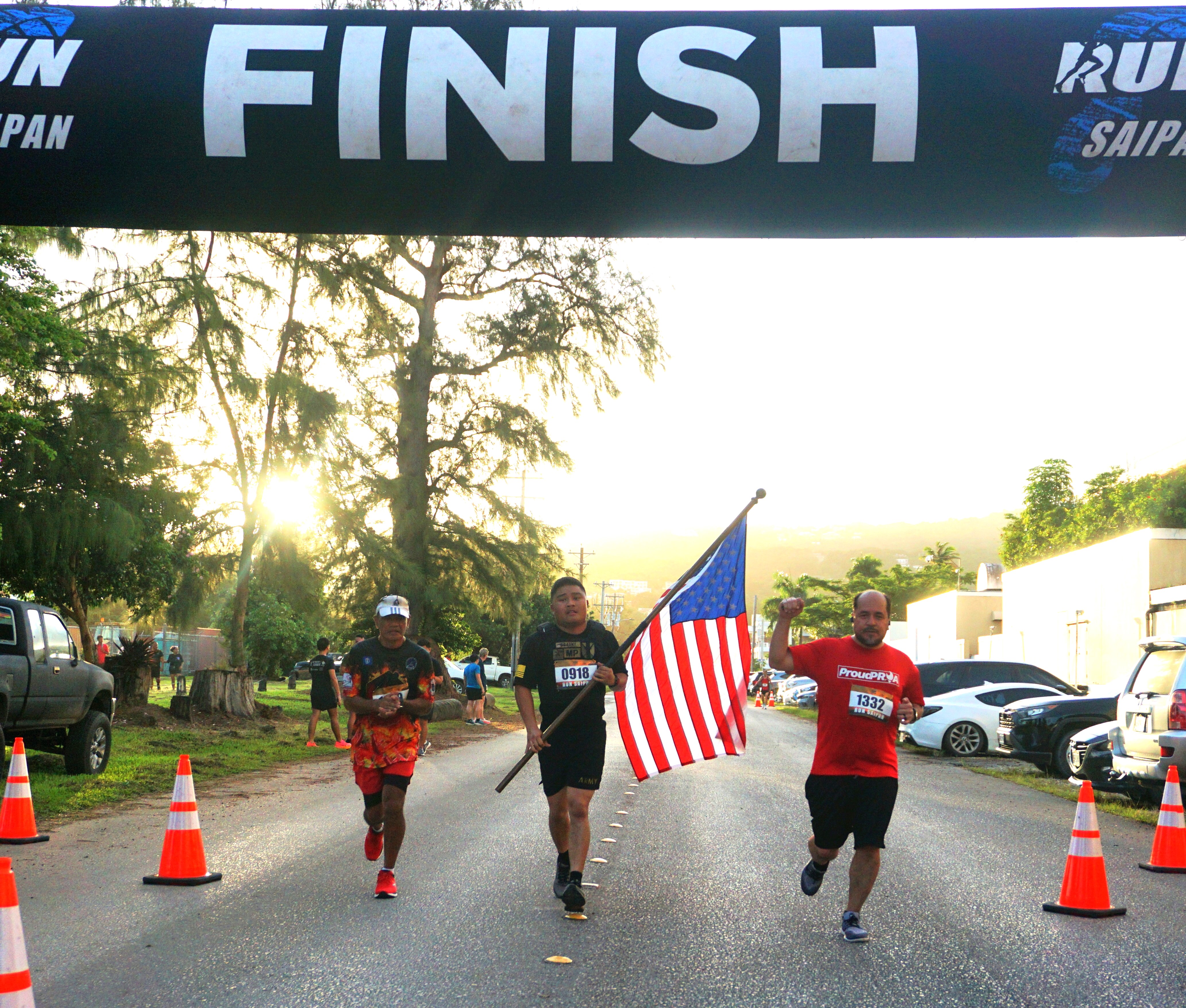 A runner holding the U.S. flag and two other participants approach the finish line of Run Saipan’s Veterans Day 5K 2024 at Micro Beach Monday morning.