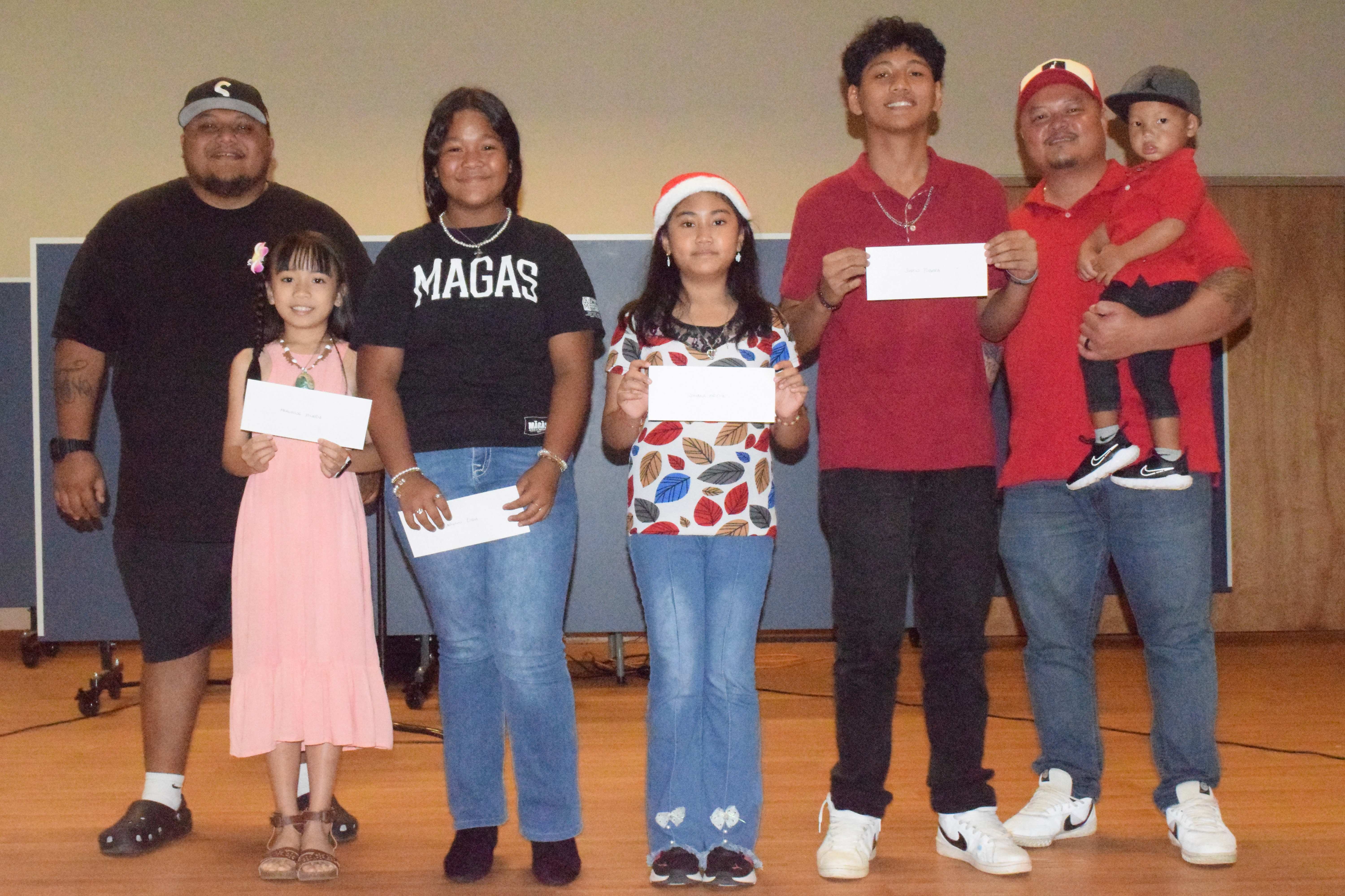 Harmony in the Community singing contest winners Francine Pineda, second left; Jaelynnn Lisua, third left; Juliana Kai Ortiz, center; and Justin Tubiera, second right, pose for a photo with Rep. Thomas John Manglona left, and Rep. Angelo Camacho and his son, at Kagman Community Center on Saturday.Photo by Emmanuel T. Erediano