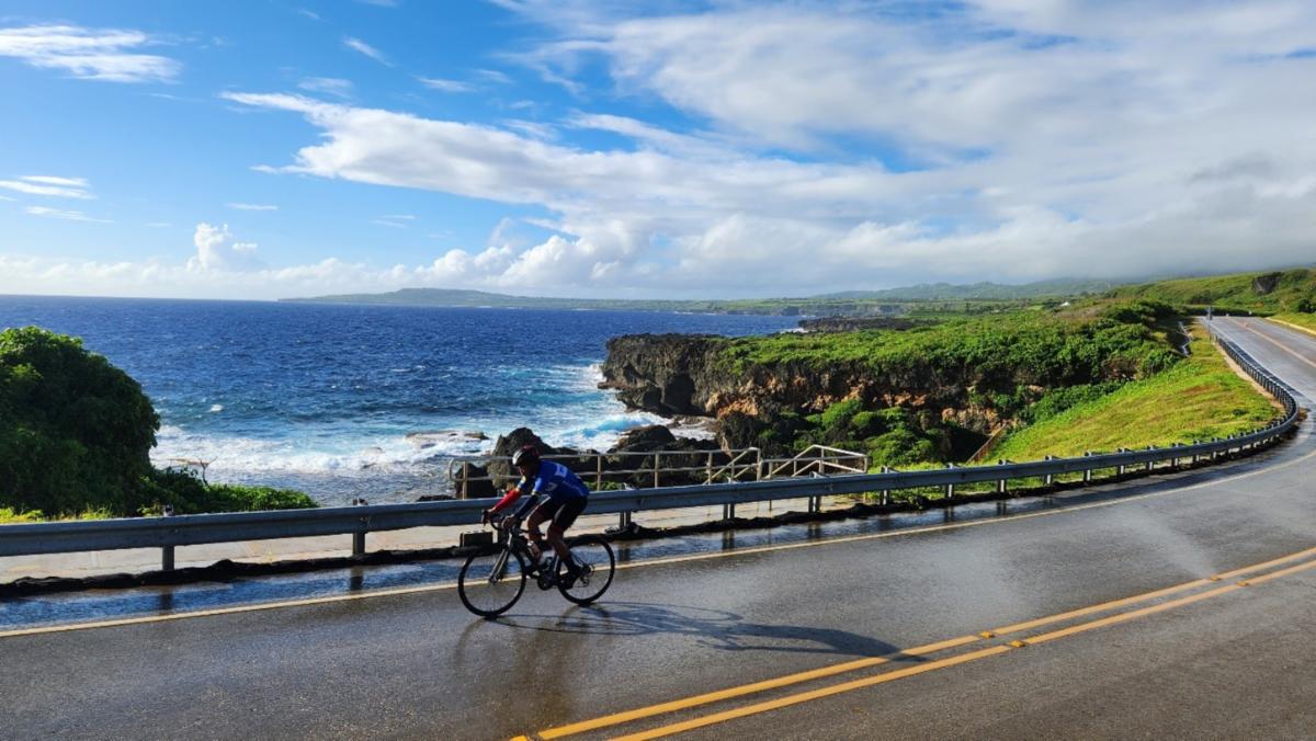 Ocean, sky, and green hills frame a biker on the course for Hell of the Marianas century cycle on Dec. 7, 2024.