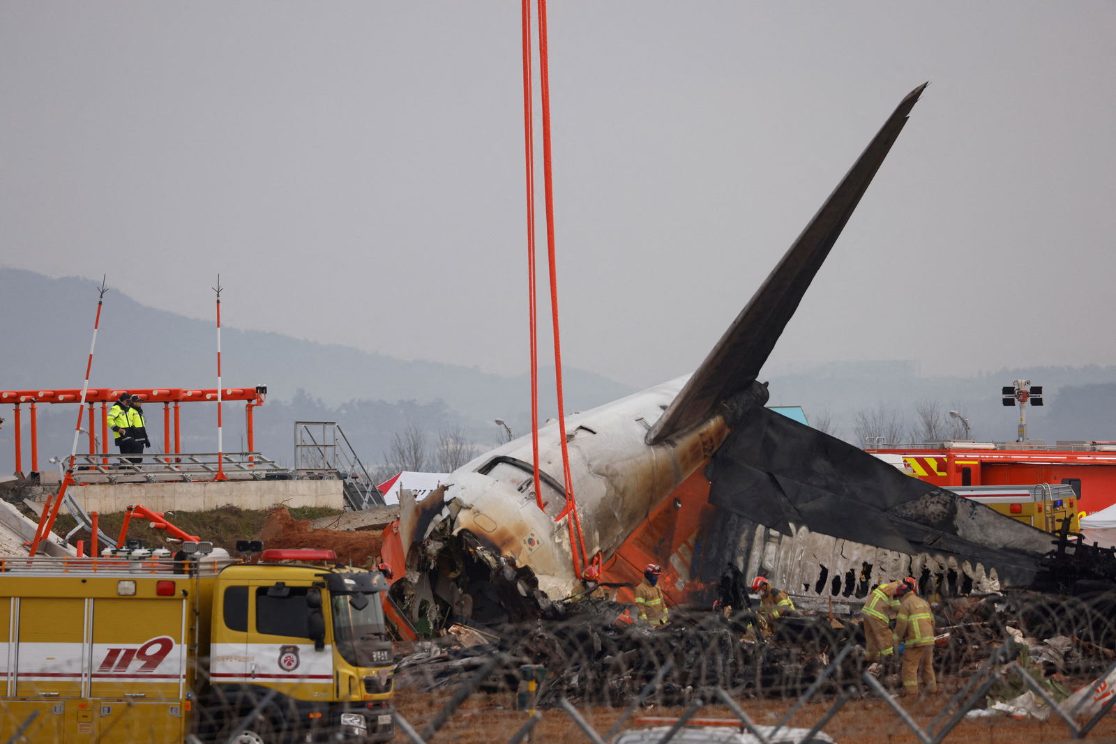 People stand as the wreckage of an aircraft lying on the ground after it went off the runway and crashed at Muan International Airport is pictured, in Muan, South Korea, Dec. 30, 2024.