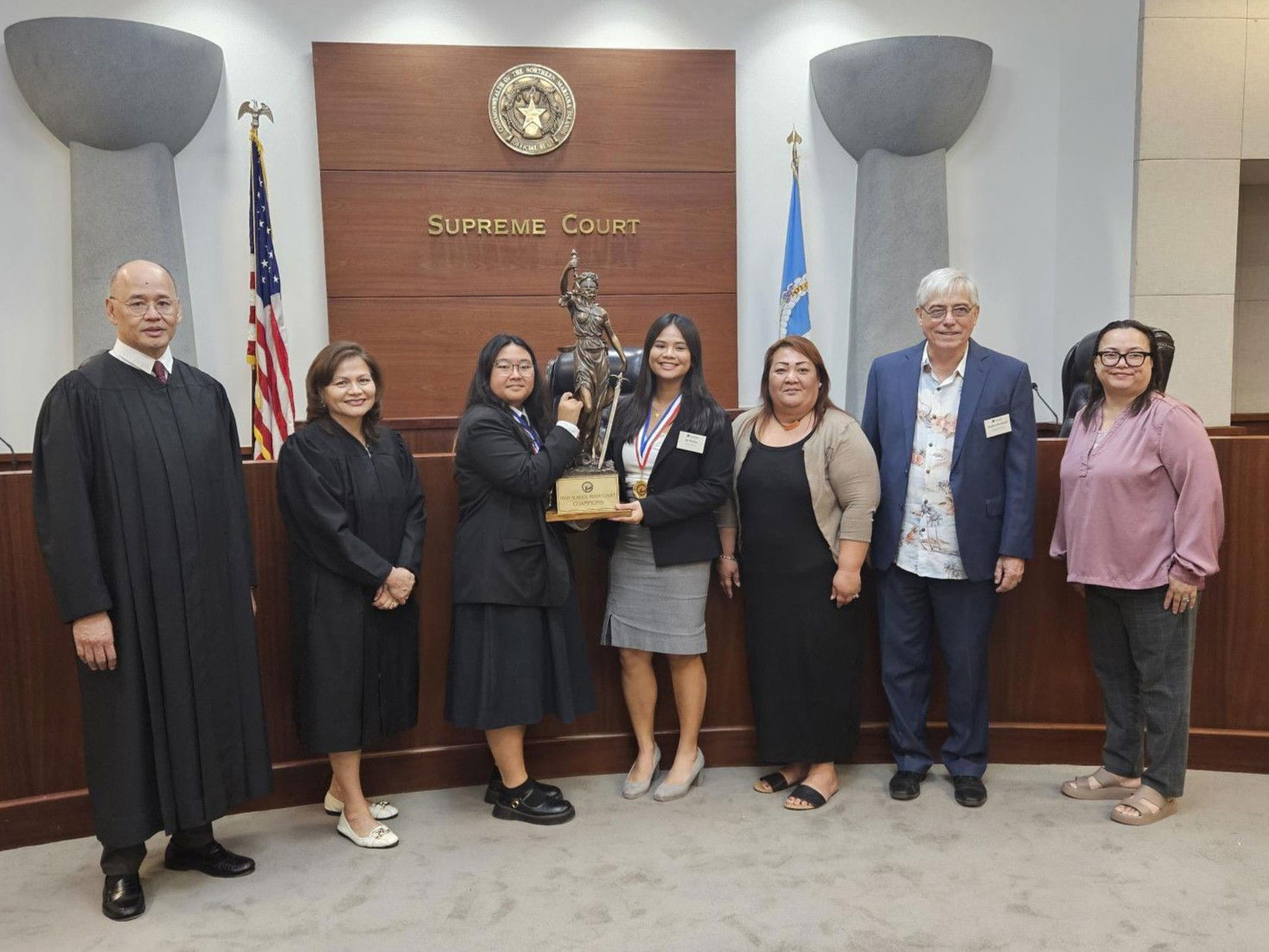 Marianas High School seniors Julia Taitano and Jia Nicdao, center, hold the Lady Hustisia perpetual trophy after winning the 2024 High School Moot Court championship on Friday, Dec.6 2024 at the Guma’ Hustisia. Also in photo are MHS coach attorney Stephen Woodruff, MHS Principal Melanie Rdiall, Melisha San Nicolas of the Public School System’s federal programs office, CNMI Supreme Court Justice John Manglona, and District Court for the NMI Chief Judge Ramona V. Manglona.