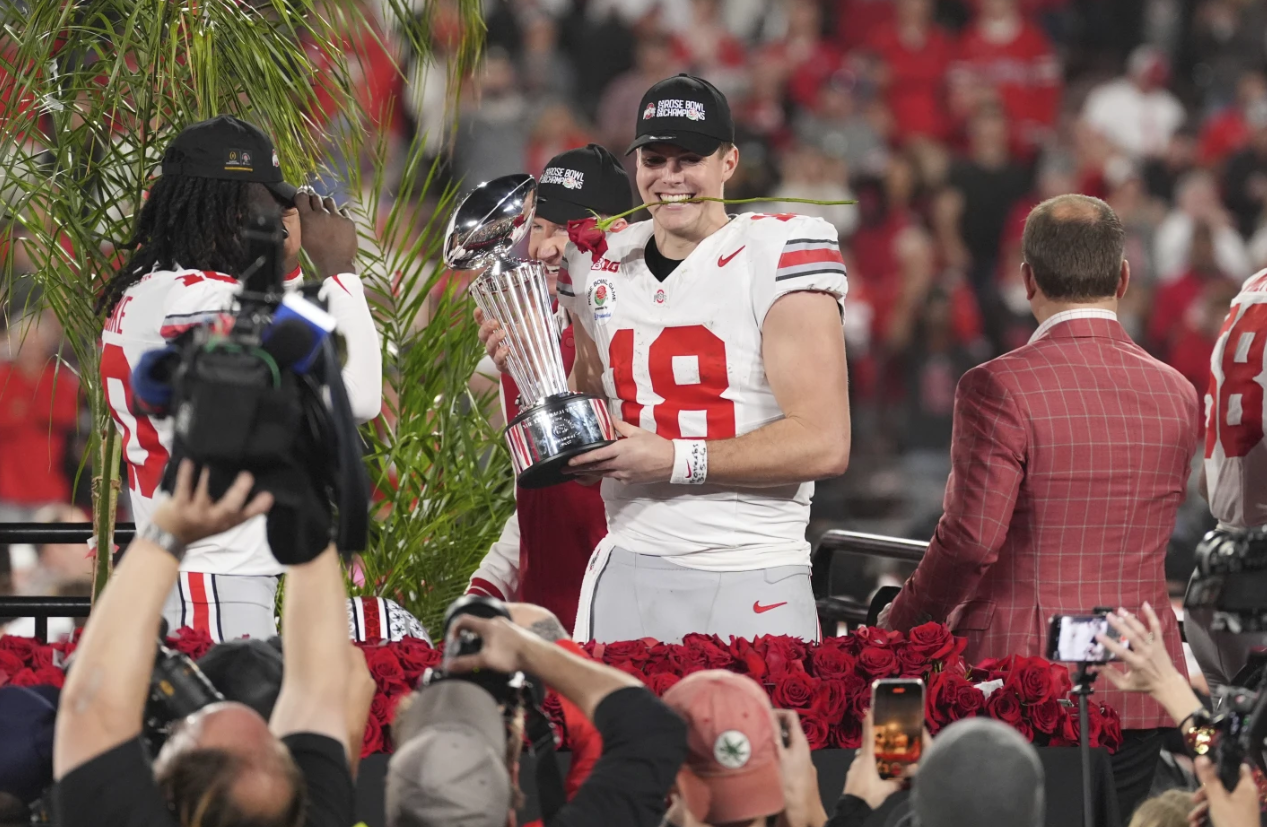 Ohio State quarterback Will Howard holds a rose in his mouth as he poses with the trophy after the team won the quarterfinals of the Rose Bowl College Football Playoff against Oregon, Wednesday, Jan. 1, 2025 in Pasadena, Calif.