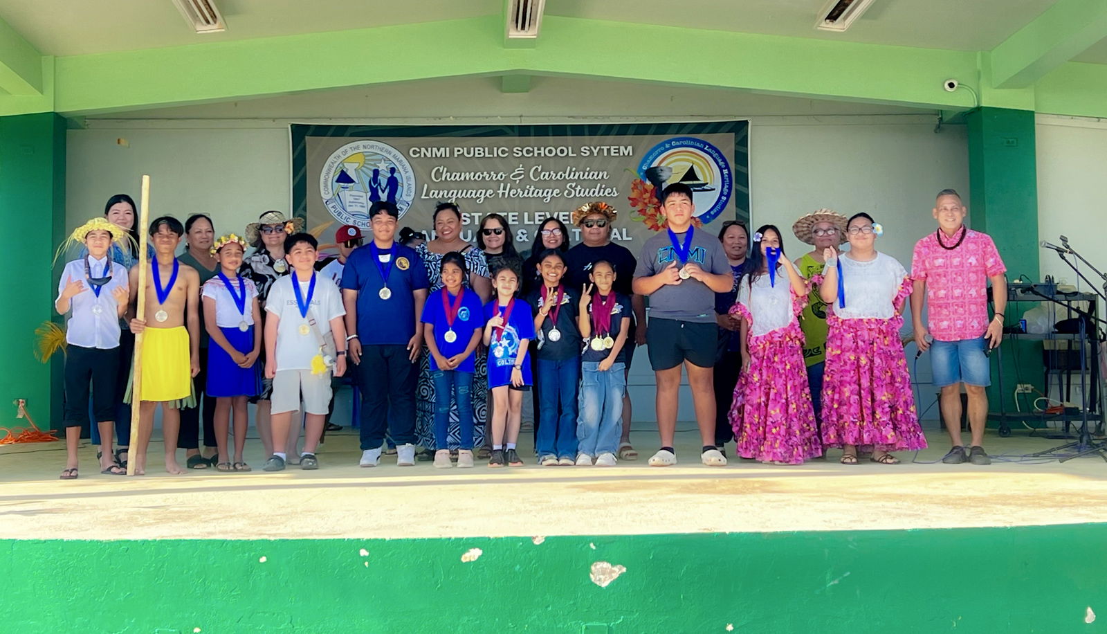 The top three winning teams in the Chamorro and Carolinian elementary storytelling competitions pose for a photo with the organizing committee led by Koblerville Elementary School Vice Principal Jonas M. Barcinas, Federal Programs Officer Jacqueline P. Che, SPED State Director Donna Flores, school principals Annette Calvo, Ben Jones, Christine Tudela, Naomi Nishimura, and Cherlyn Osung.