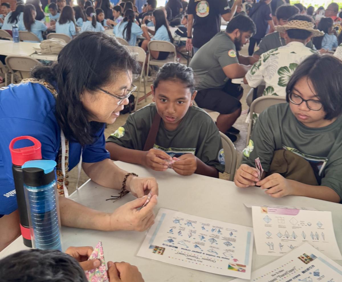 Motono Higuchi of the Japanese School of the Japanese Society of the Northern Mariana Islands teaches students of MY WAVE Clubs how to make paper cranes during the Marianas Tourism Education Council Tourism Summit on Jan. 24, 2025, at Garapan Central Park in Saipan. The clubs will fold 1,000 origami cranes to mark 80 years of peace in The Marianas since World War II.