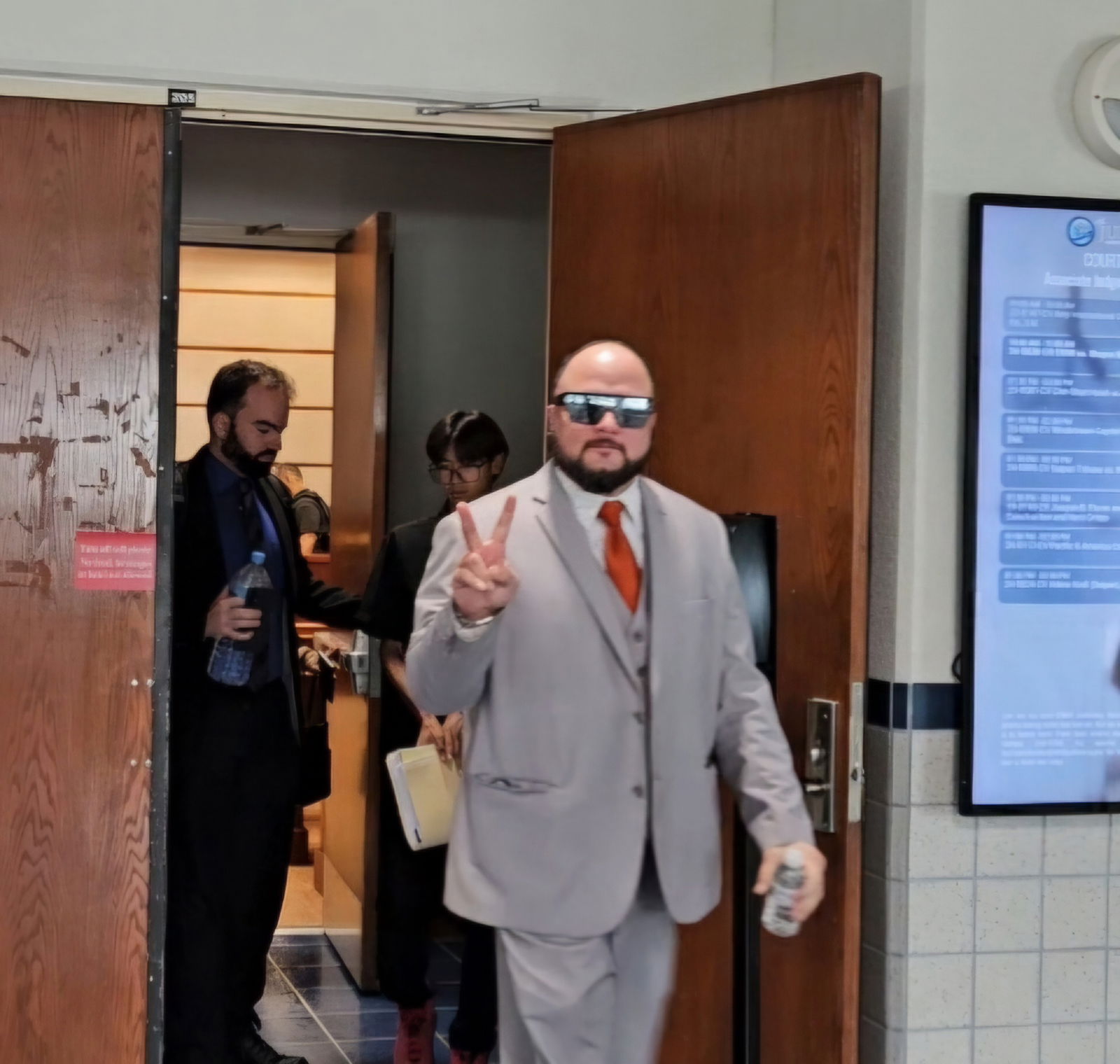 Shayne Villanueva flashes the “peace” sign as he exits the courtroom following a hearing at the Guma’ Hustisia on Nov. 19. 2024. Also in photo is his lawyer, Keith Chambers II, left.