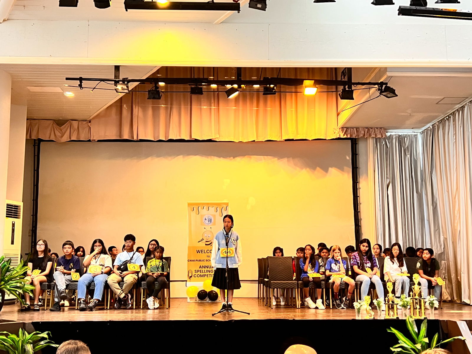 A speller takes center stage as her fellow competitors look on.