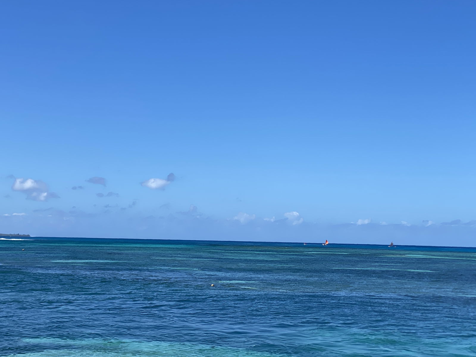 The double-hulled canoe Semantic, with its orange sail, sails alongside Anåguan, with its brown sail, toward Tinian.