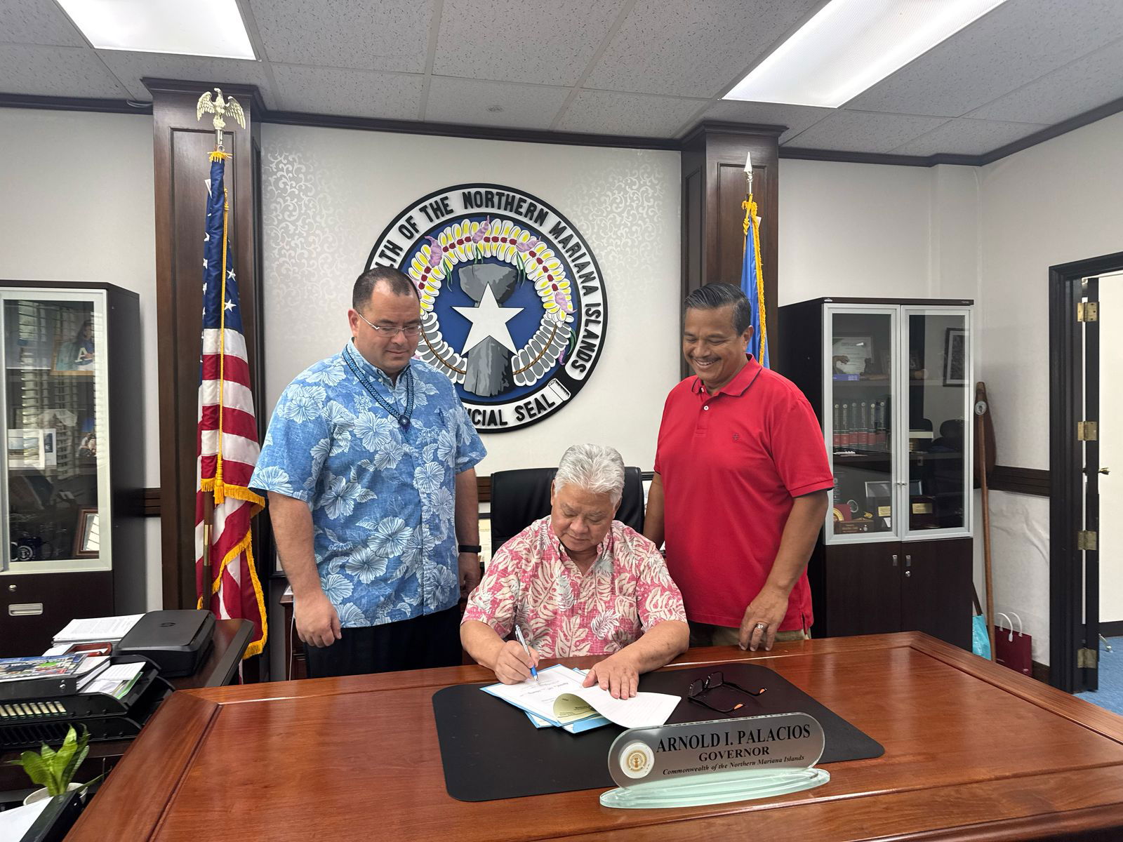 Gov. Arnold I. Palacios signs the revised fiscal year 2025 budget as Speaker Edmund S. Villagomez and Senate Fiscal Affairs Committee Chair Jude U. Hofschneider look on.Office of the Governor photo