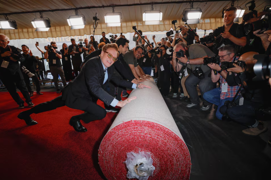 Academy Awards host Conan O'Brien pushes the rolled red carpet during its rollout for the 97th Academy Awards in Los Angeles, California, Feb. 26, 2025.REUTERS